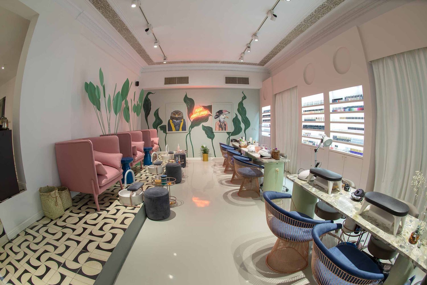 Modern nail salon with patterned floor, pink velvet chairs, and potted plants decorating the bright interior space.