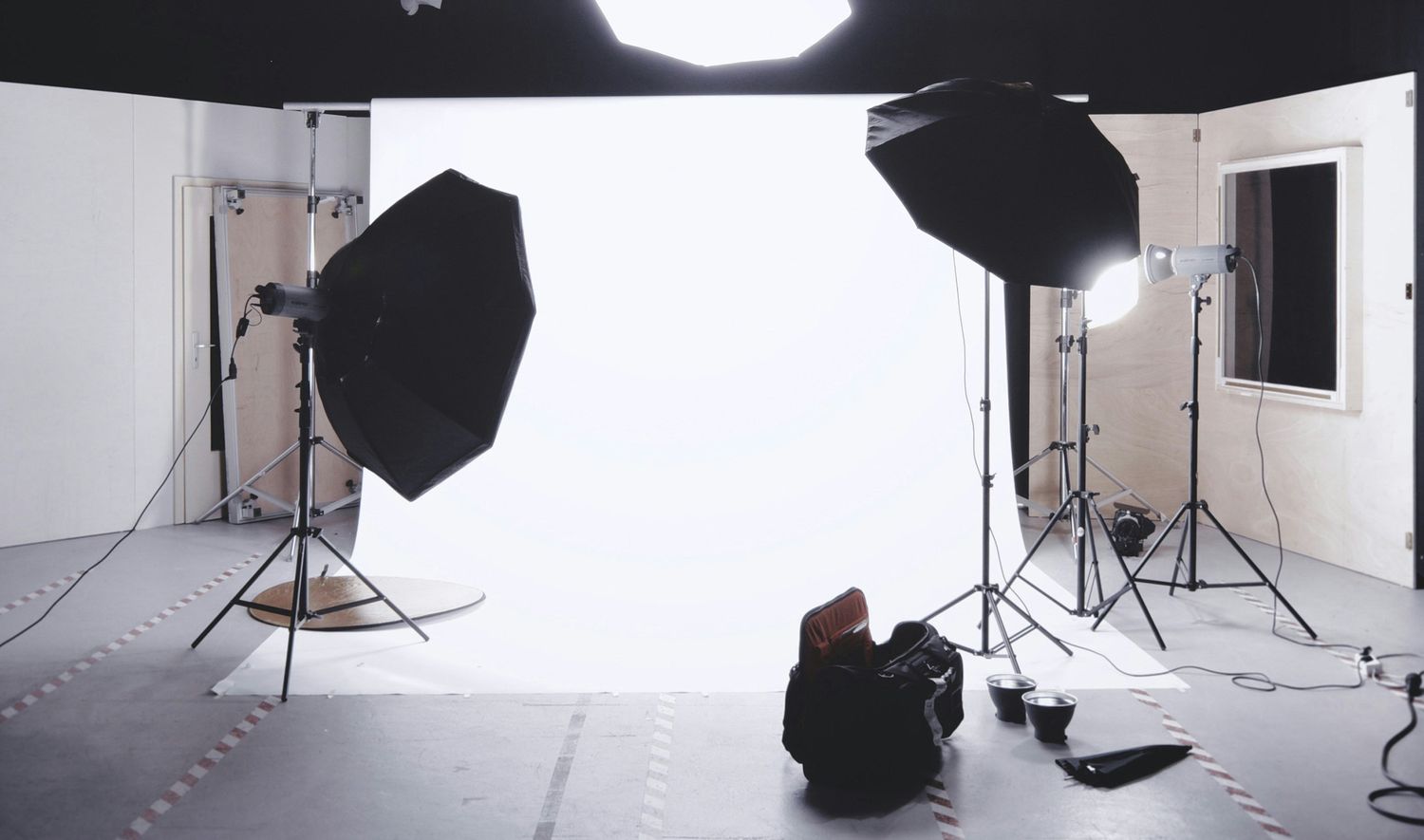 Professional photography studio setup with white backdrop, lighting equipment and softboxes in a clean interior space.