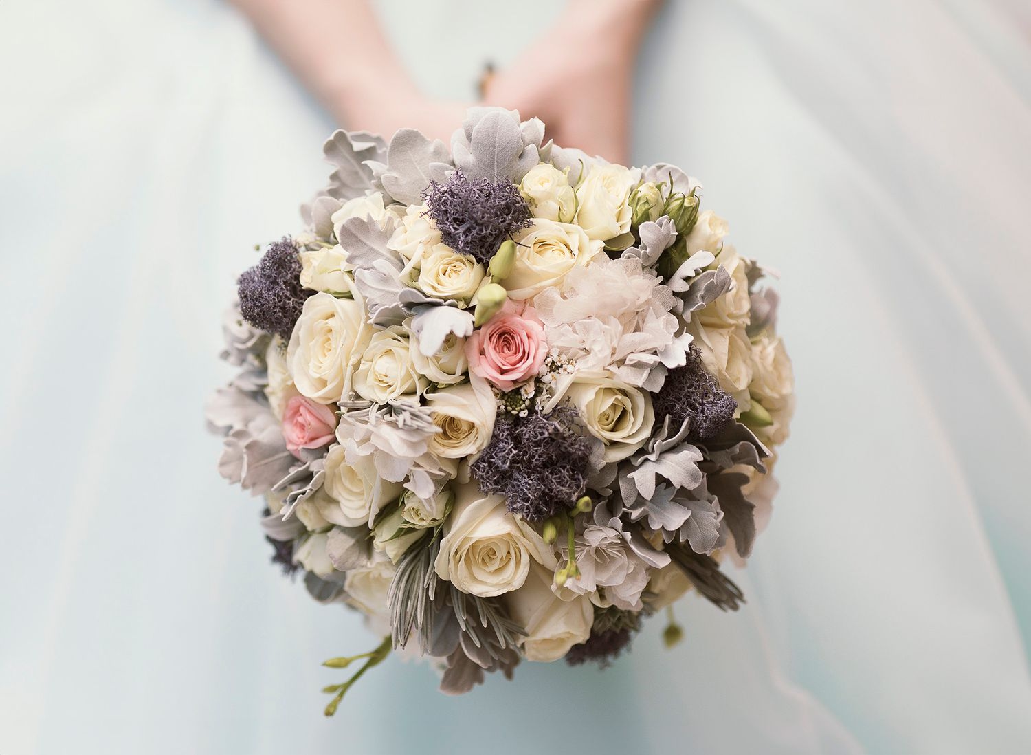 Elegant bridal bouquet with cream roses, pink accents and dusty grey foliage arranged in a romantic vintage style.