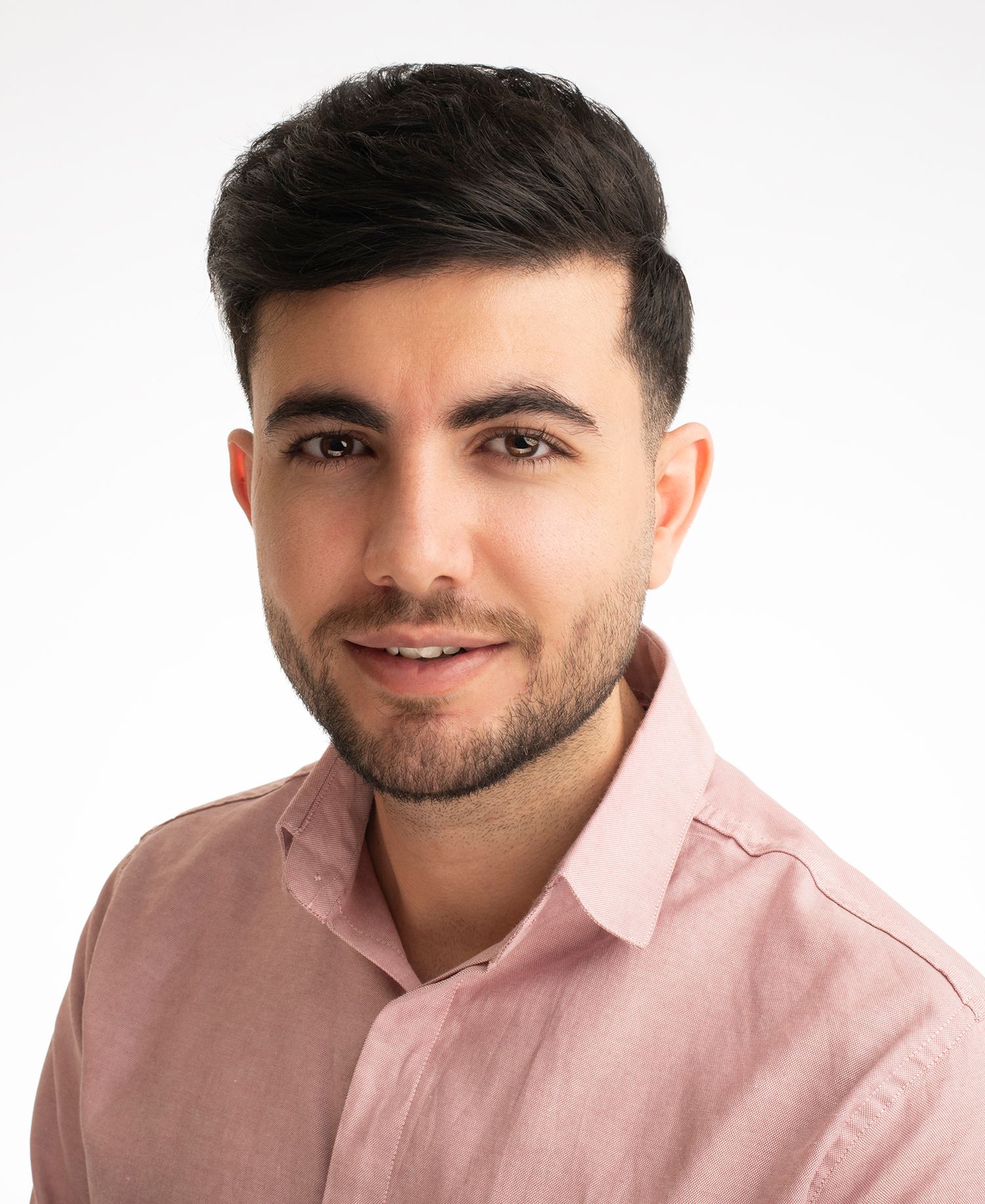 Professional headshot of a young man in a pink dress shirt smiling against a white background taken in west Los Angeles.