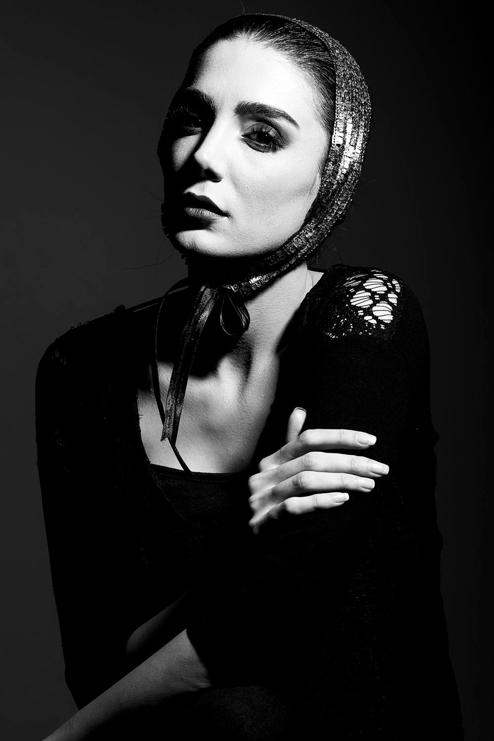 Black and white portrait of an elegant woman in a black top and headscarf, posing dramatically in studio lighting.