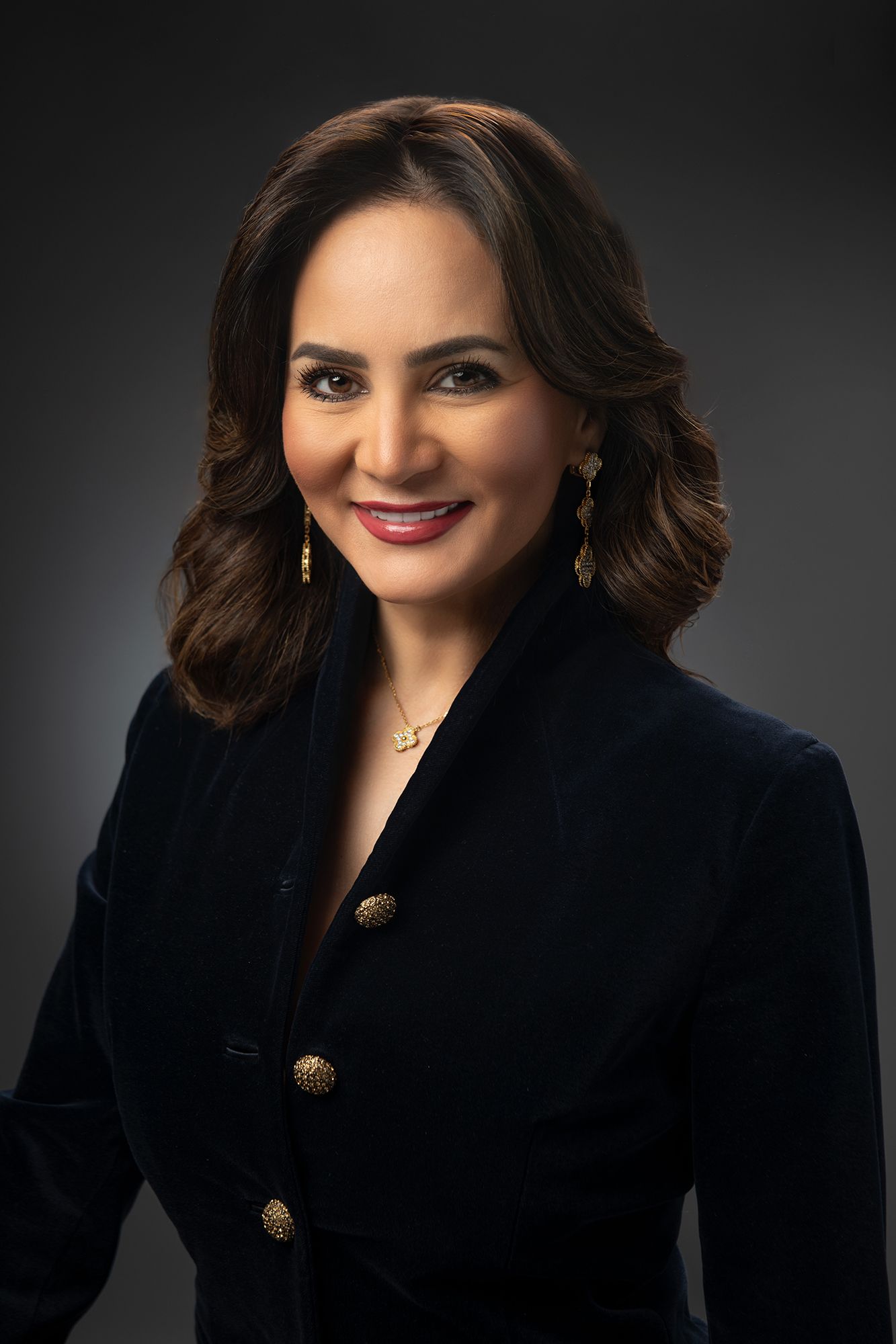 Professional headshot of entrepreneur Bita MIlanian in black blazer with gold buttons against dark backdrop taken in west los angeles.