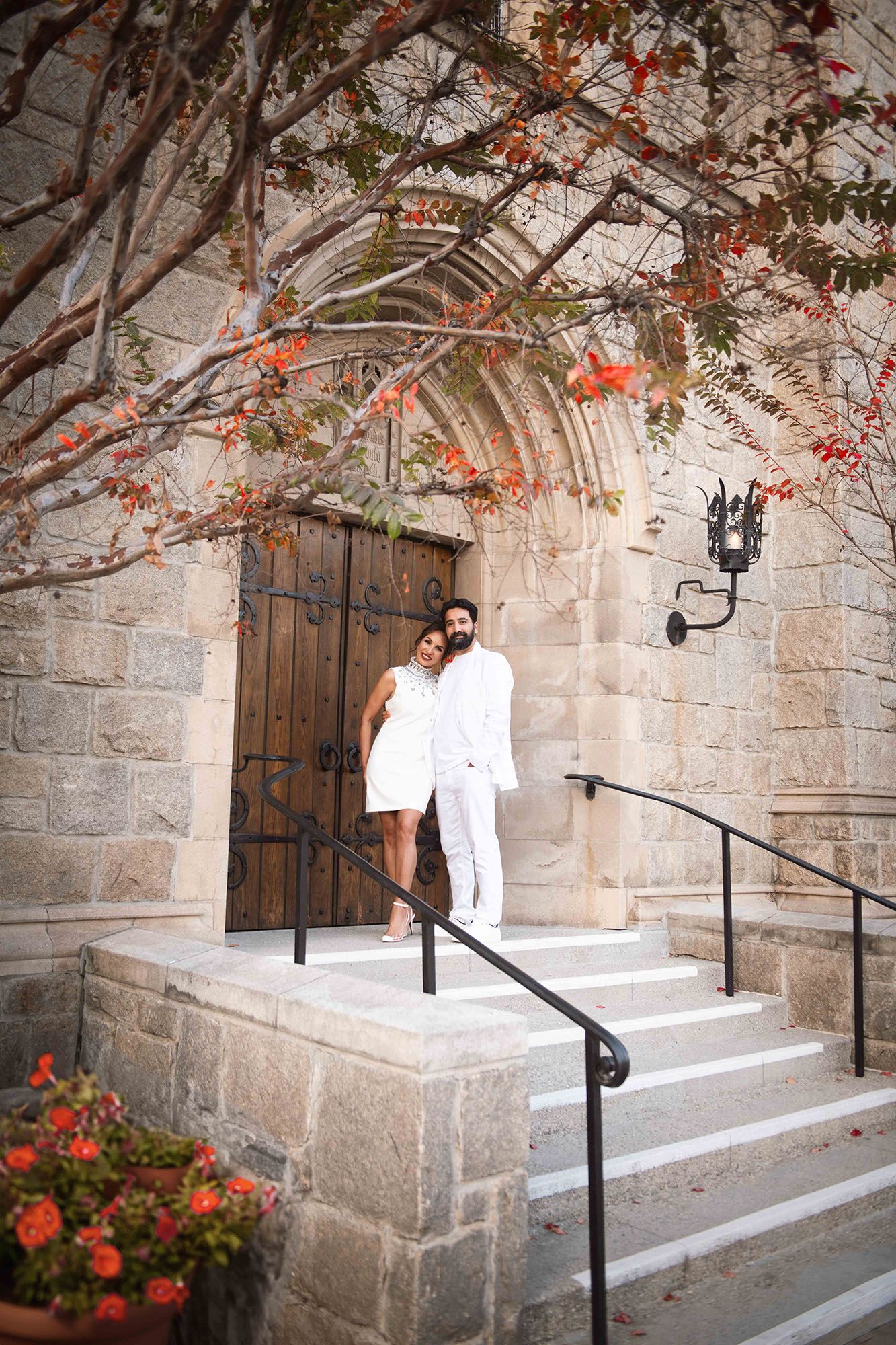 Stone archway entrance with white steps, black metal handrails, and orange flowers blooming overhead.