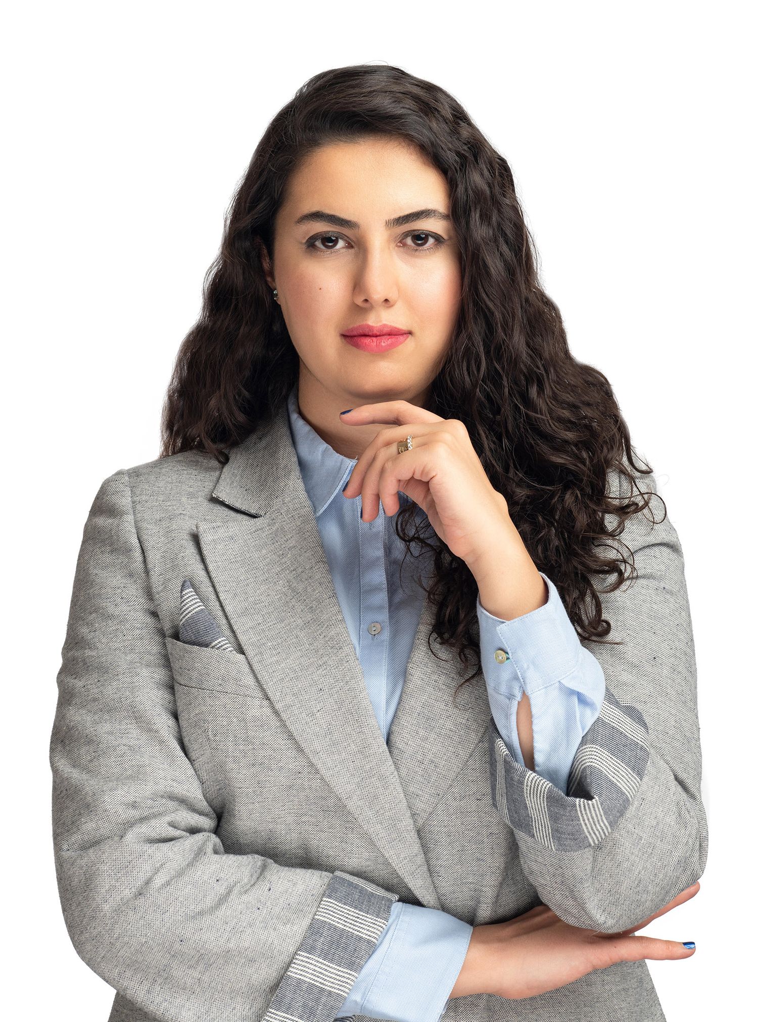 Professional portrait of someone in a light gray blazer and blue button-down shirt with long dark curly hair.