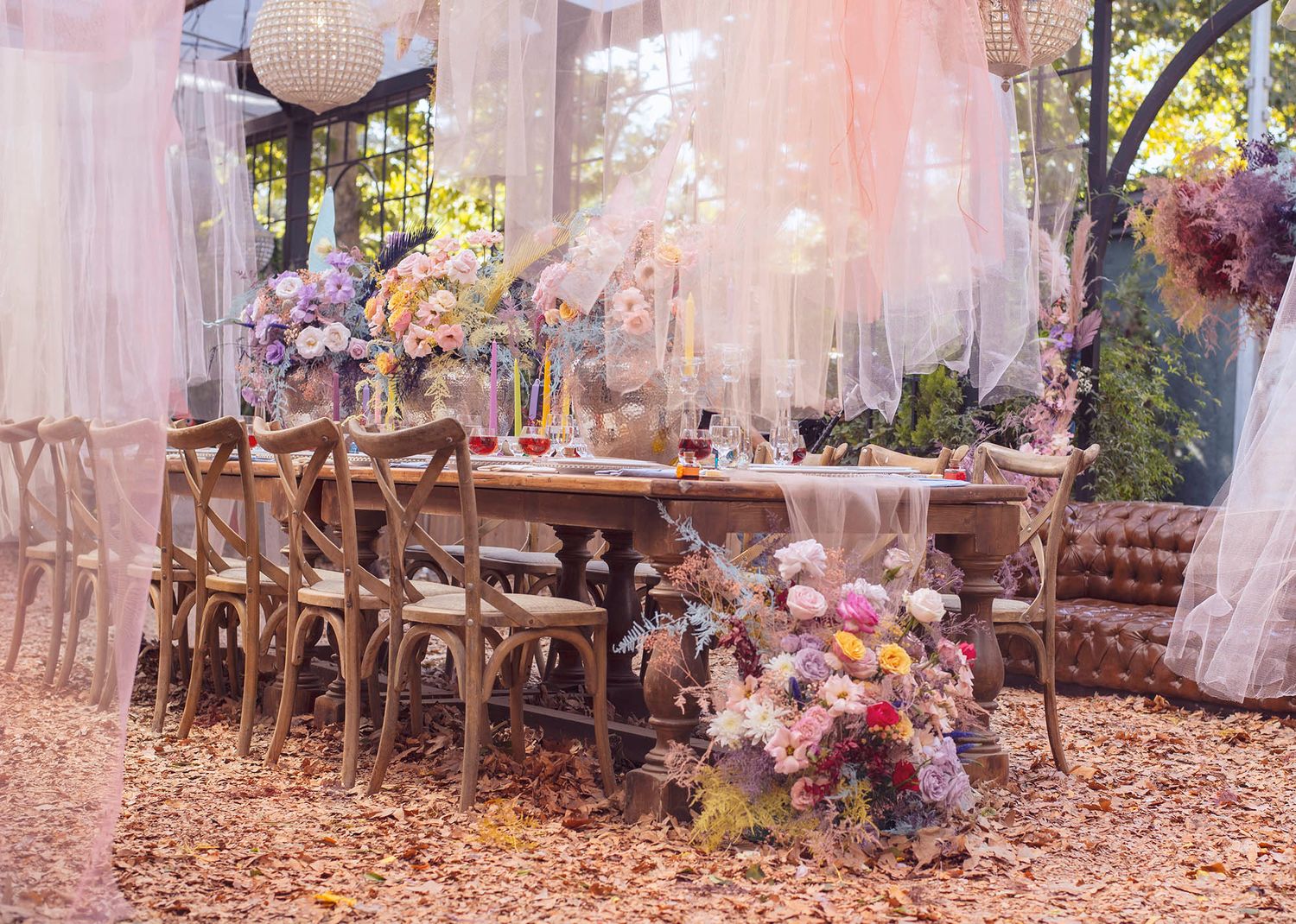 A rustic outdoor table setting with vintage chairs and pink floral decorations in a dreamy autumn garden scene.
