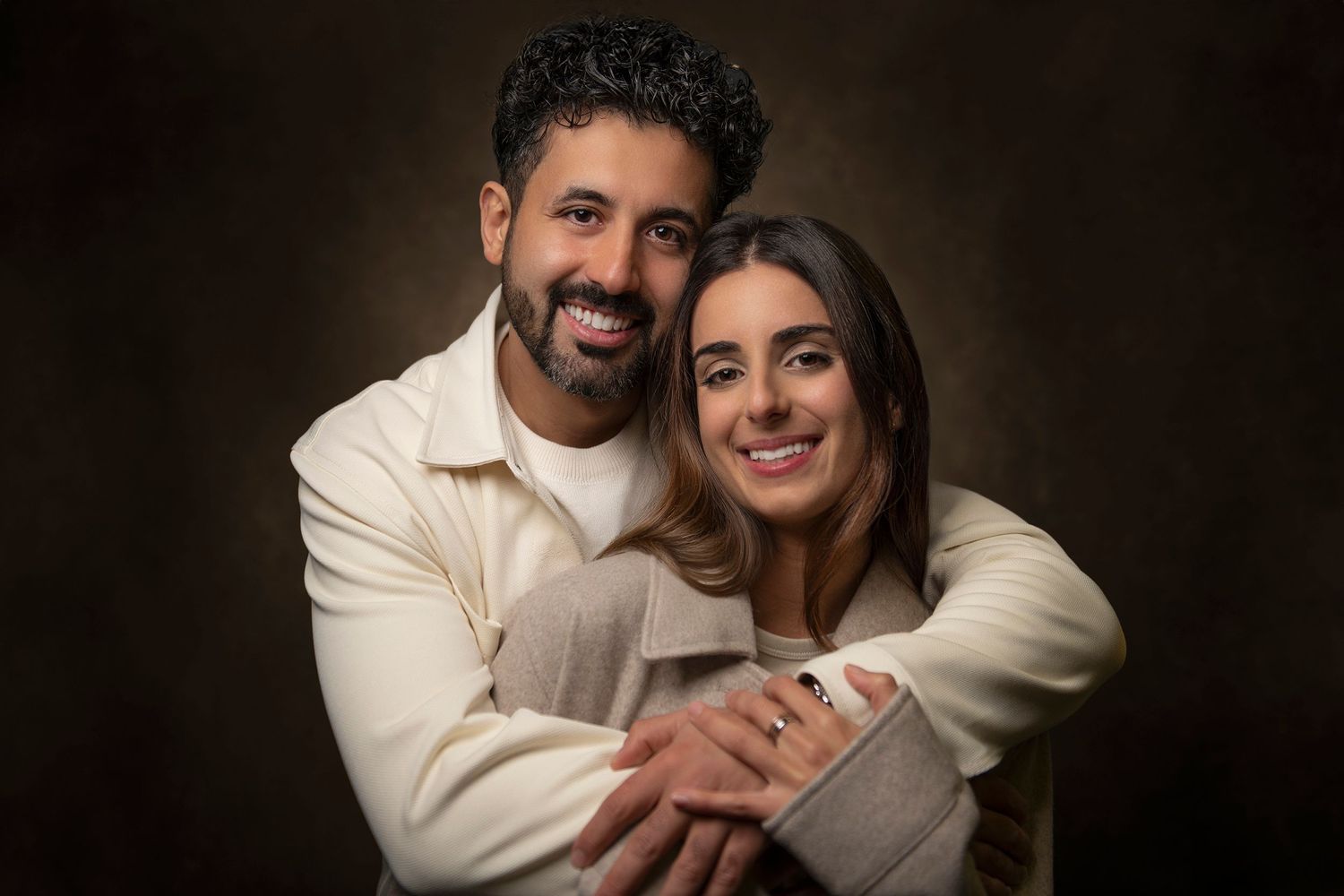A series of sweet and intimate couple photos with matching cream-colored outfits in front of a dark backdrop.