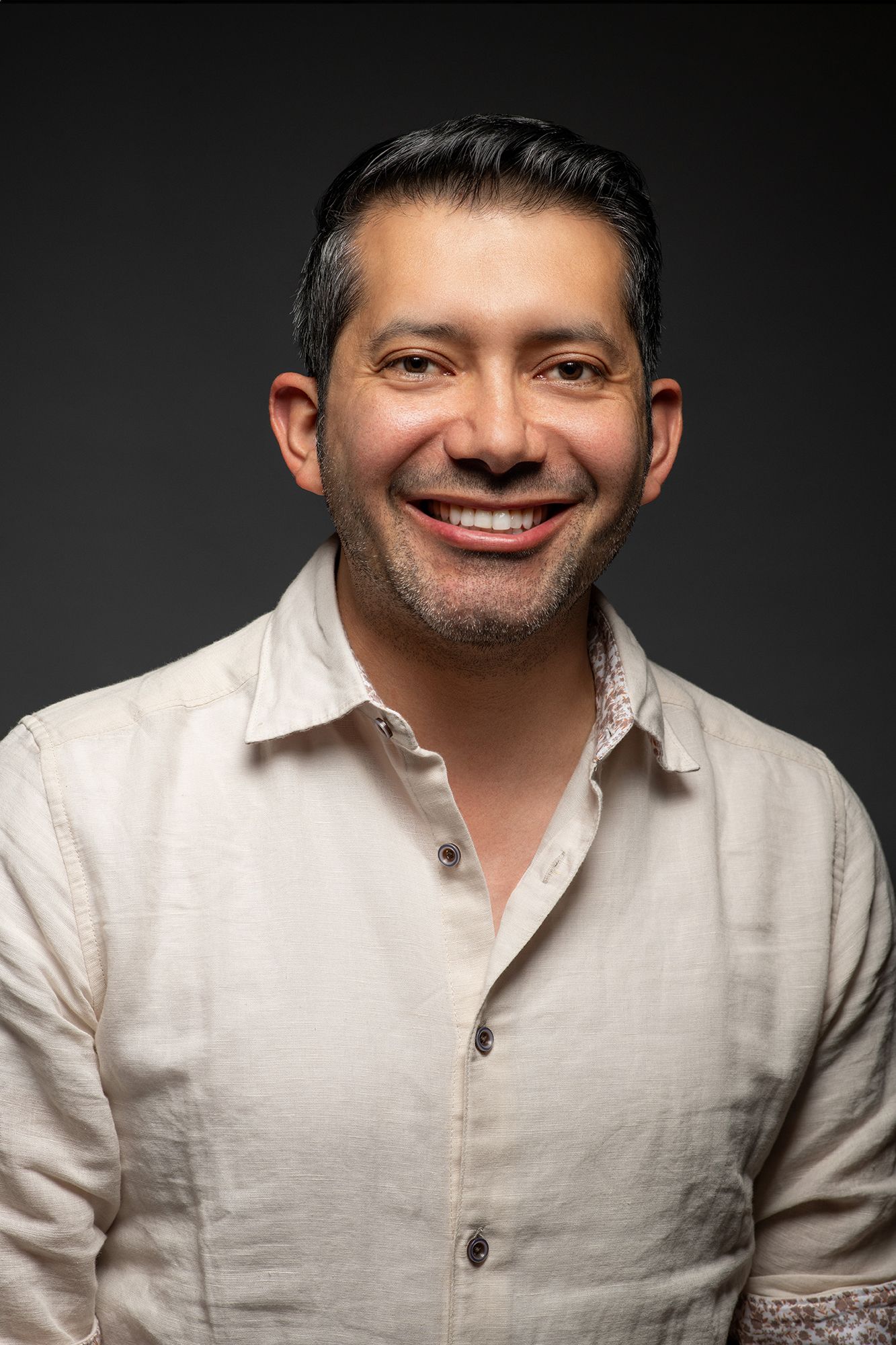 Professional commercial portrait and headshot of person in white linen shirt with genuine smile against dark background taken in west LA.