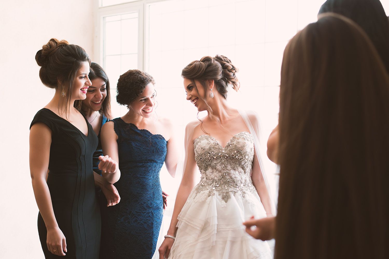 A wedding party getting ready in a bright room with bridesmaids in blue dresses and a bride in white.