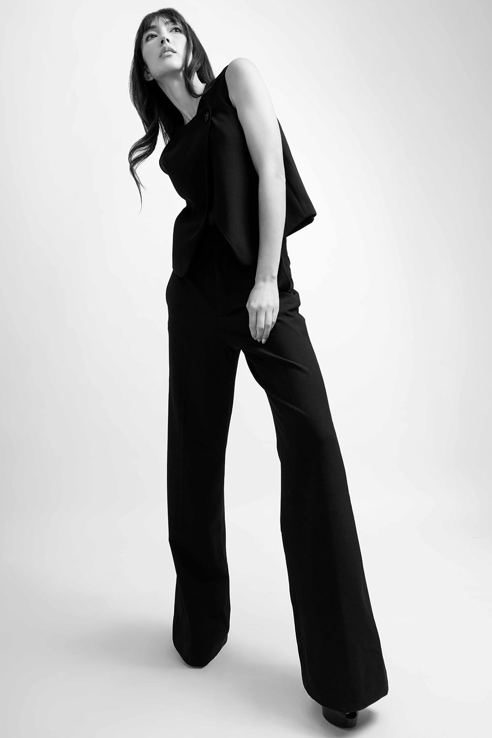 Black and white photo of a woman in wide-leg black trousers and sleeveless top, posing elegantly in a studio.