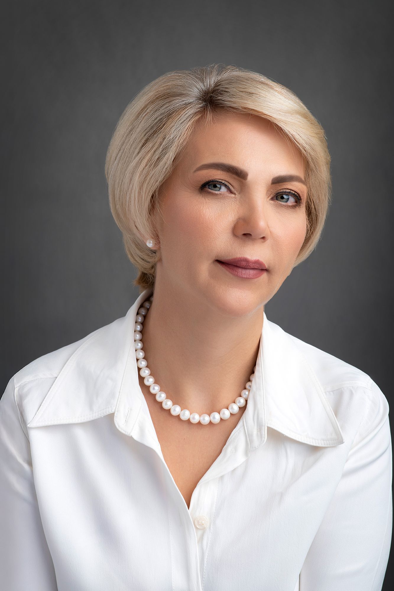 Elegant businesswoman headshot and portrait in white blouse wearing pearl necklace against dark background taken in west Los Angeles.