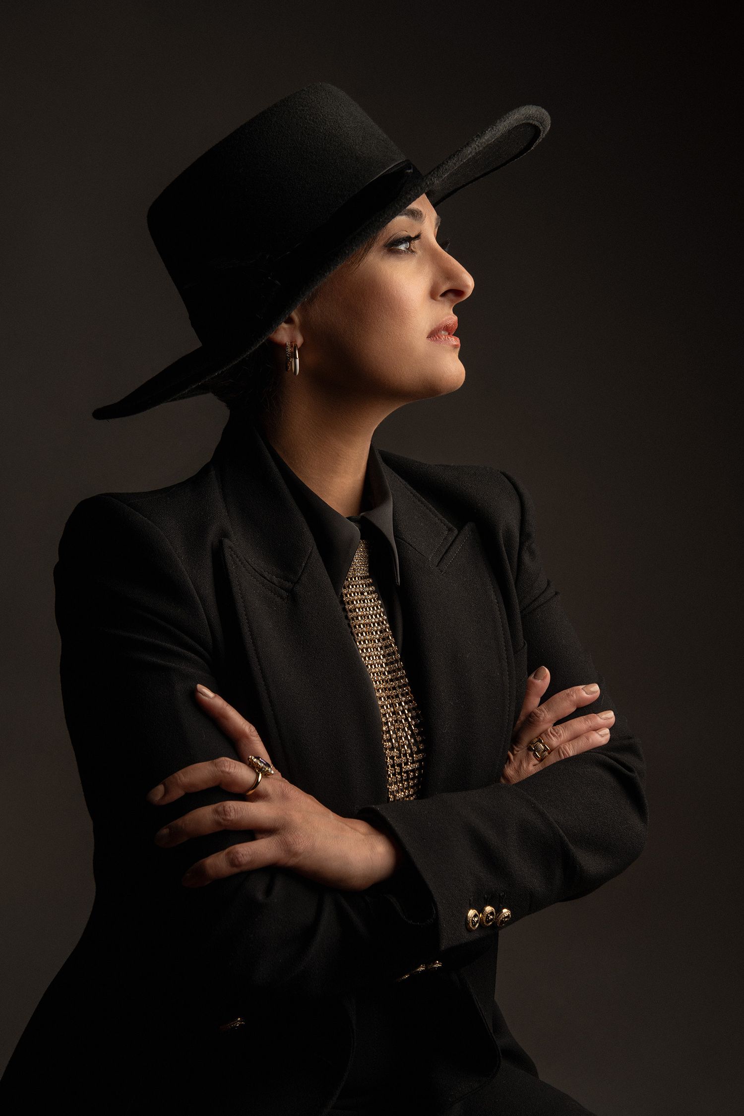 Artistic portraits showing persian pop singer Rana Mansour in black suit and gold accessories against shadowy backdrop.