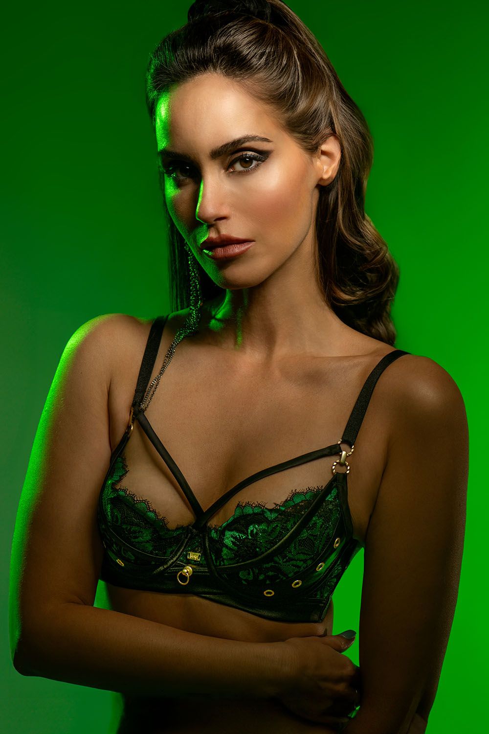 Woman in green lace bralette posing against vibrant green studio background with dramatic lighting.