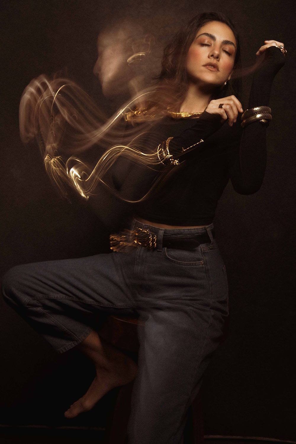 Woman dancing with a golden sword surrounded by light trails on a dark background.