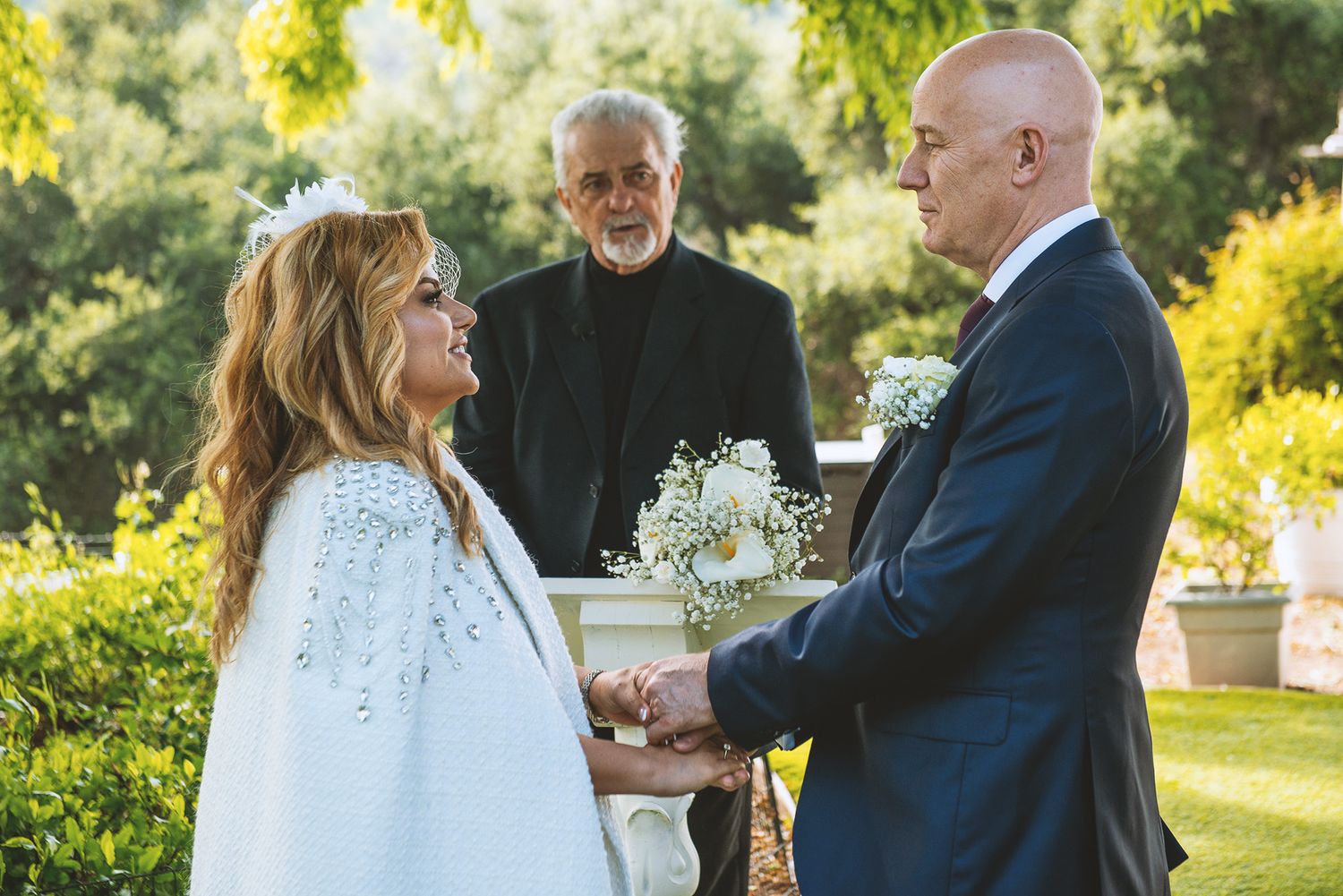 A couple shares a romantic dance outdoors in a garden setting during a wedding celebration.
