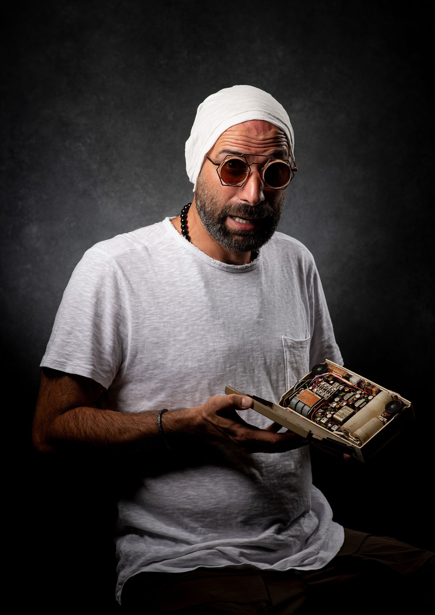 persian podcaster and comedian Farshid Manafi in casual attire reading and reacting expressively to a book in studio setting. headshot