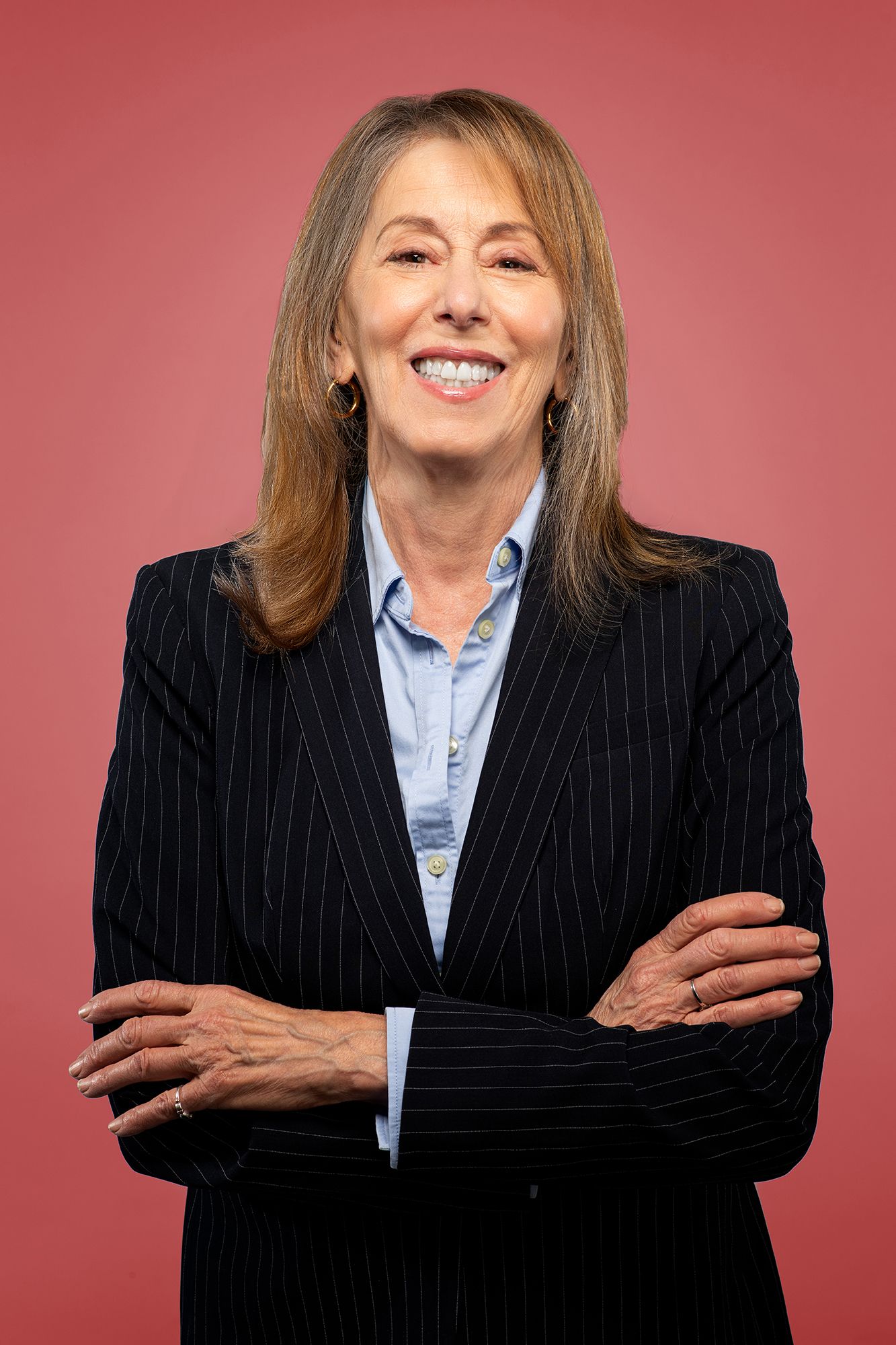 Professional casting headshot of smiling businesswoman in pinstripe suit against red backdrop taken in west Los Angeles.