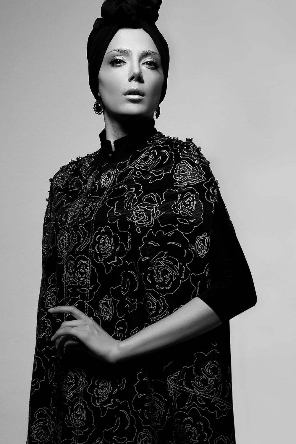 Black and white portrait of a woman in a floral embroidered cape with an elegant head wrap.