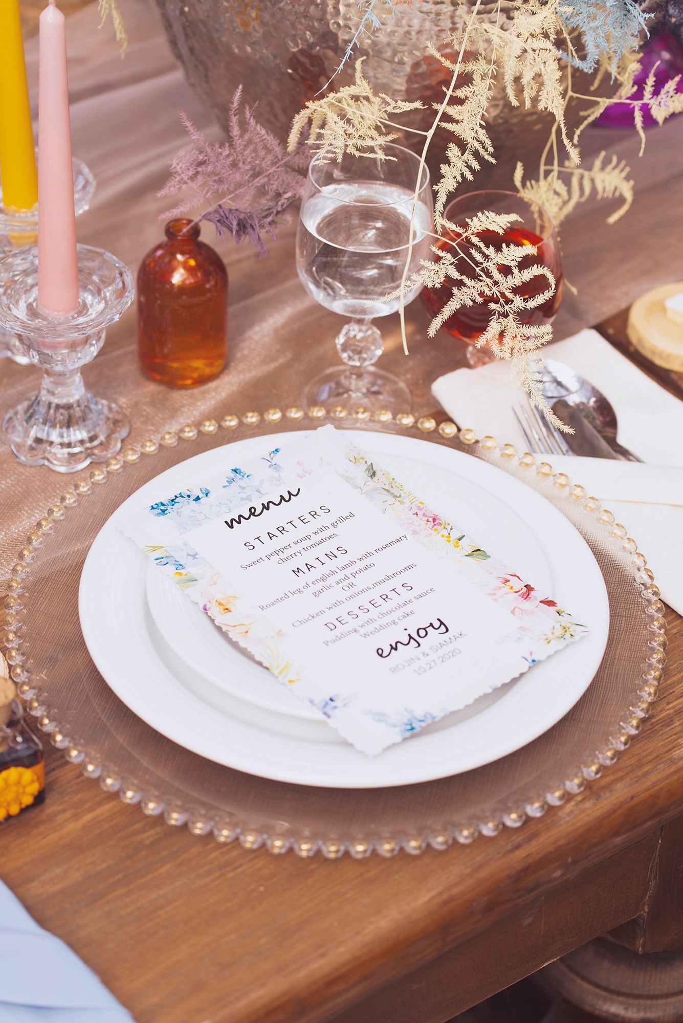 Elegant place settings with floral menu cards on wooden tables at a wedding reception with beaded charger plates.