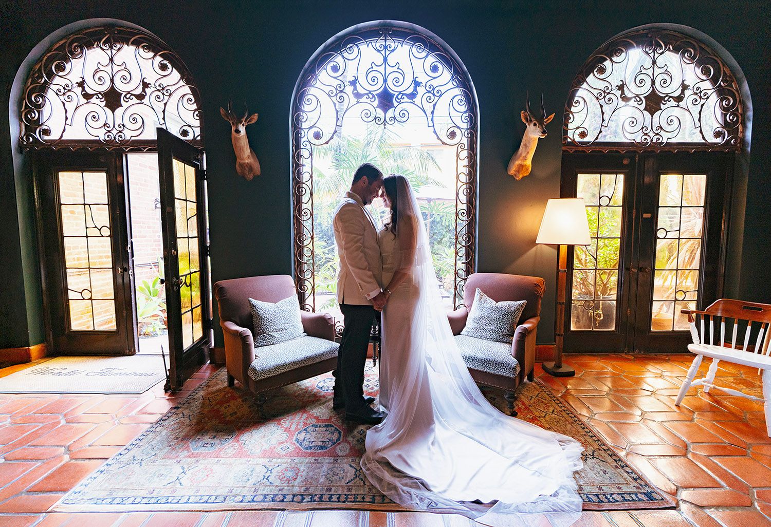 Silhouetted figures in wedding attire pose against backlit stained glass windows in a romantic church setting.