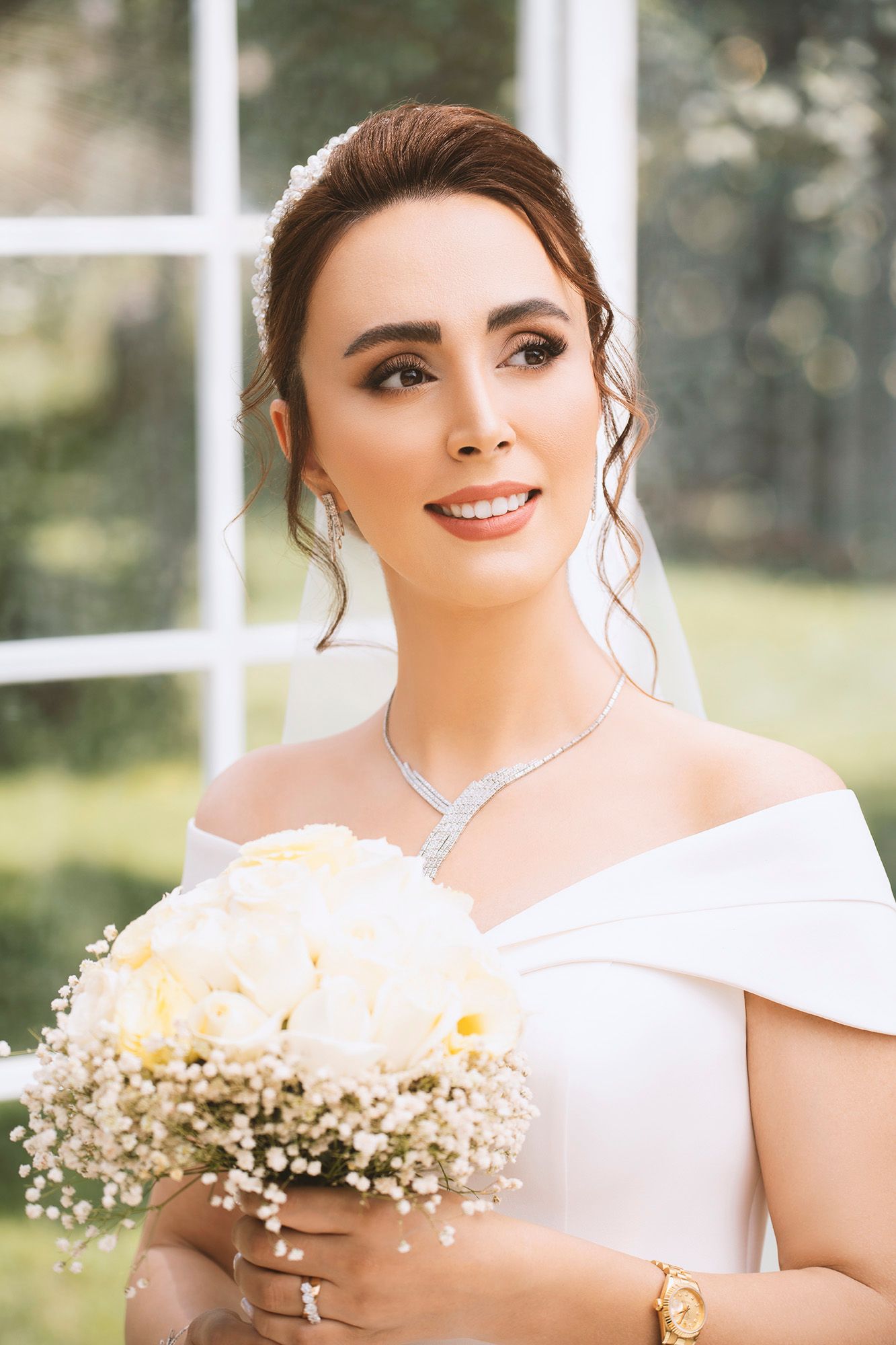 A bride in a white dress holds a delicate bouquet of baby's breath flowers in an outdoor setting.