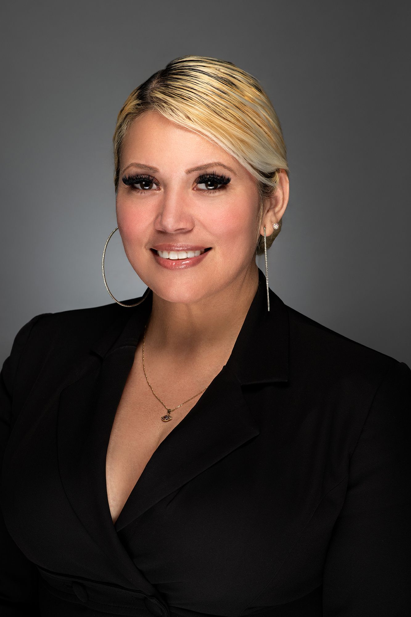 Studio portrait and headshot of person in black blazer with blonde hair and hoop earrings against grey backdrop taken in west Los Angeles.