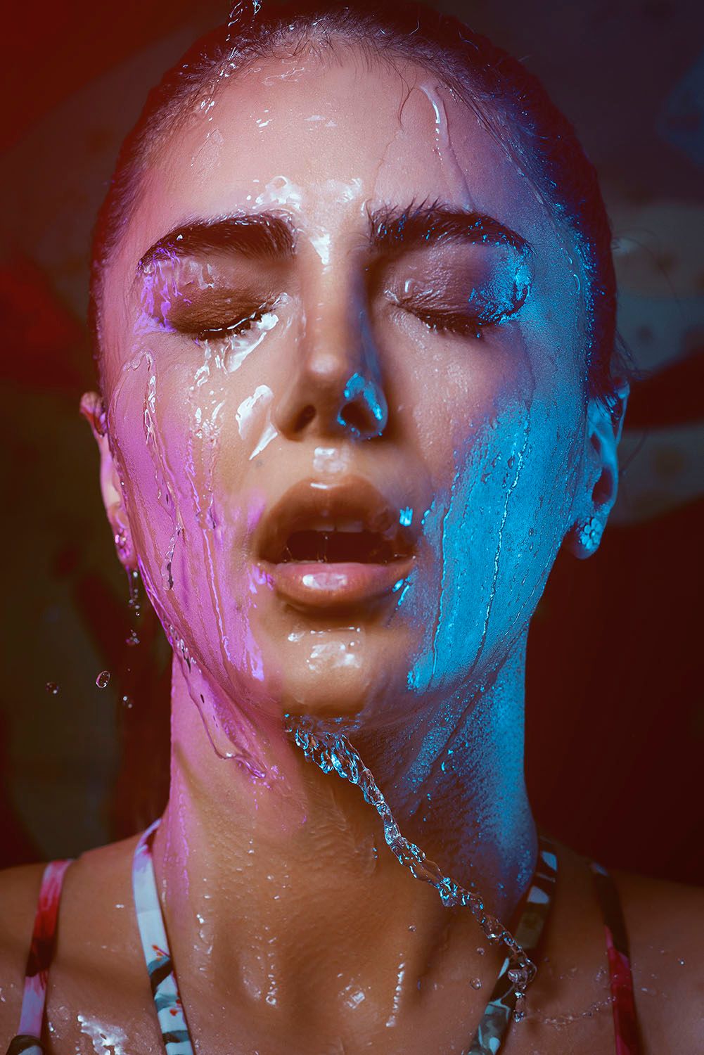 Close-up portrait of woman with colorful paint dripping down her face under neon lights.