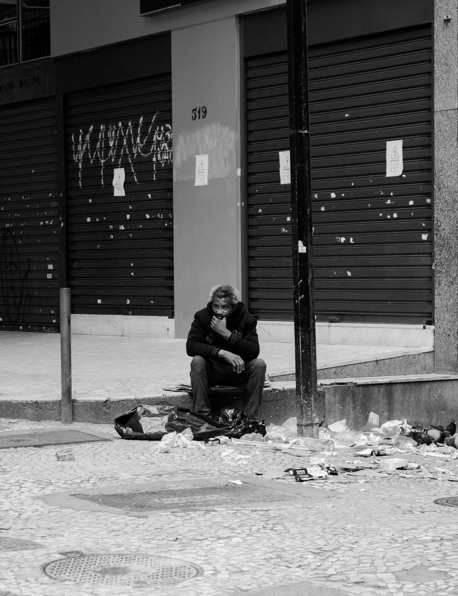 Black and white street photo of person sitting alone among urban debris.