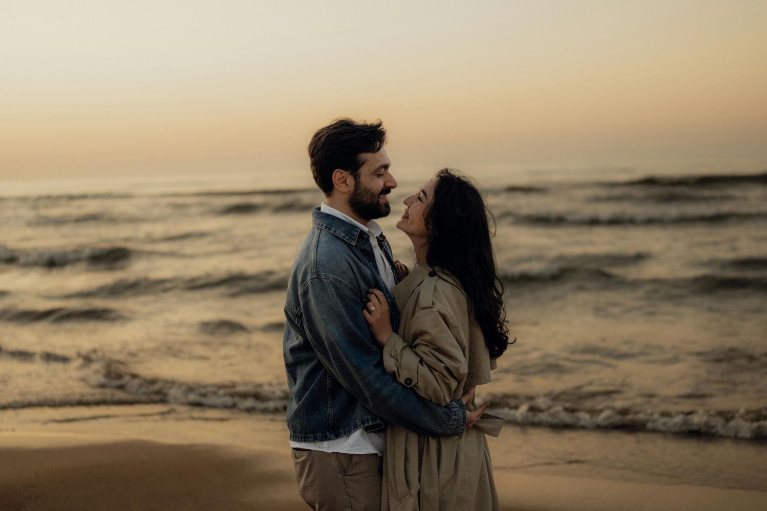 Romantic couple embracing on beach during golden hour sunset.