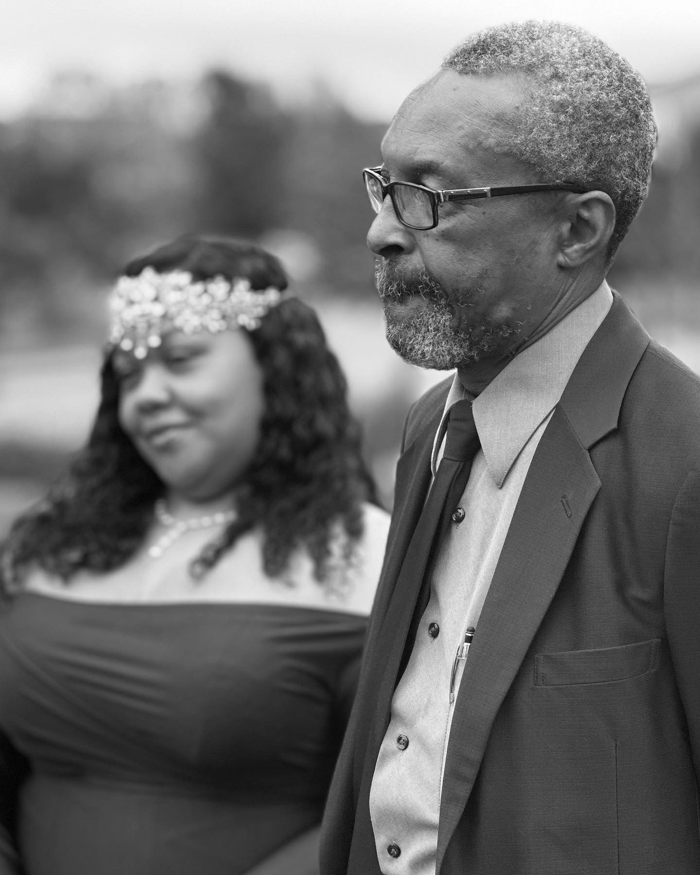 Elegant black and white portrait of a couple in formal attire at an outdoor event.