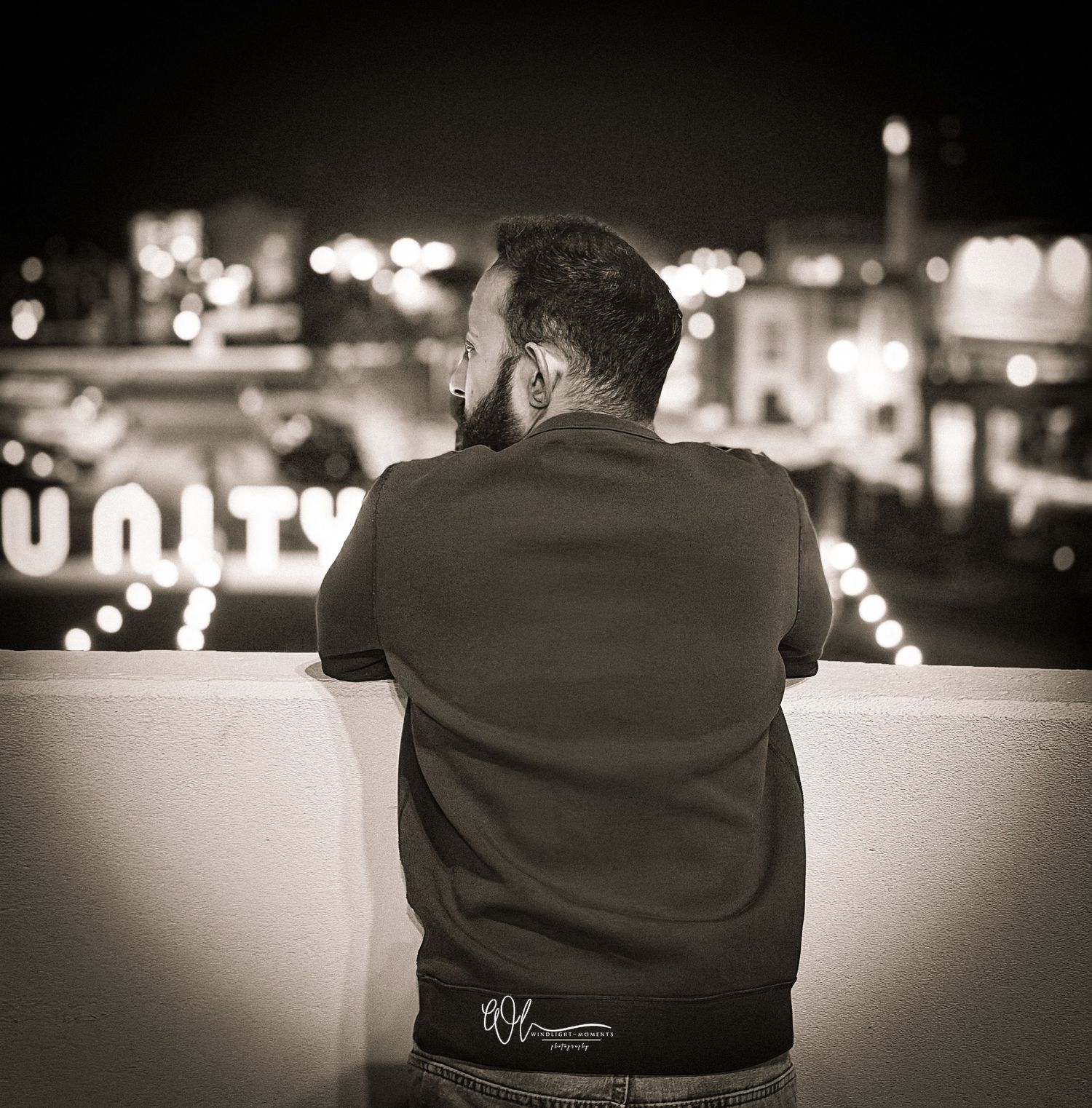 Black and white panoramic sequence showing a person sitting alone on a bench at night with city lights in background.