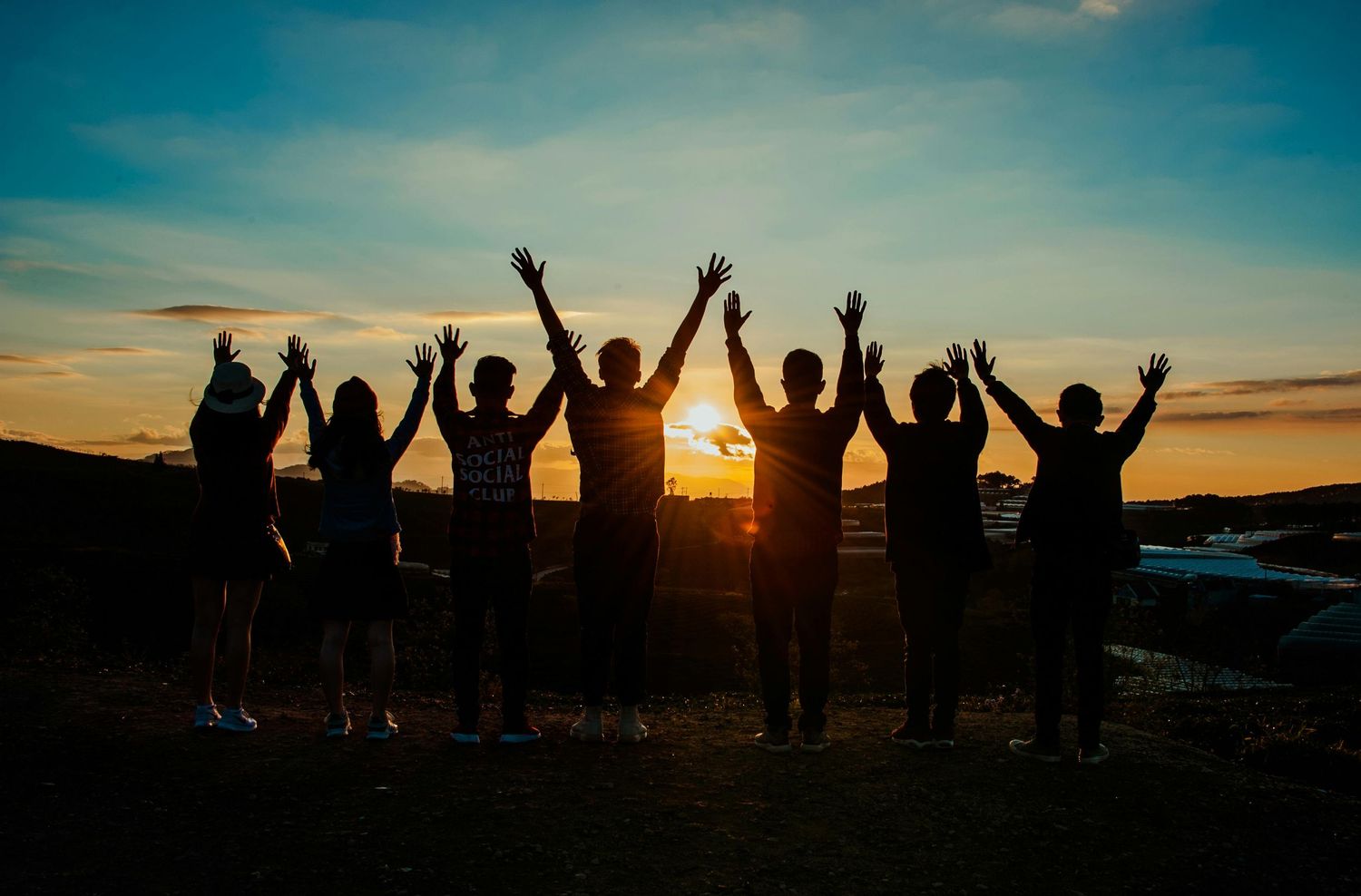 Silhouettes of people with raised arms celebrating against a dramatic sunset sky.