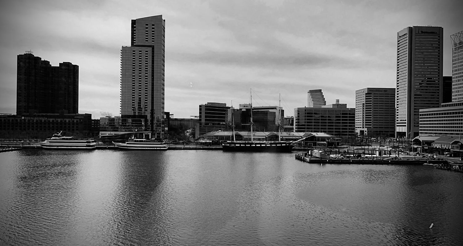 Black and white panoramic cityscape showing a waterfront skyline with modern buildings.
