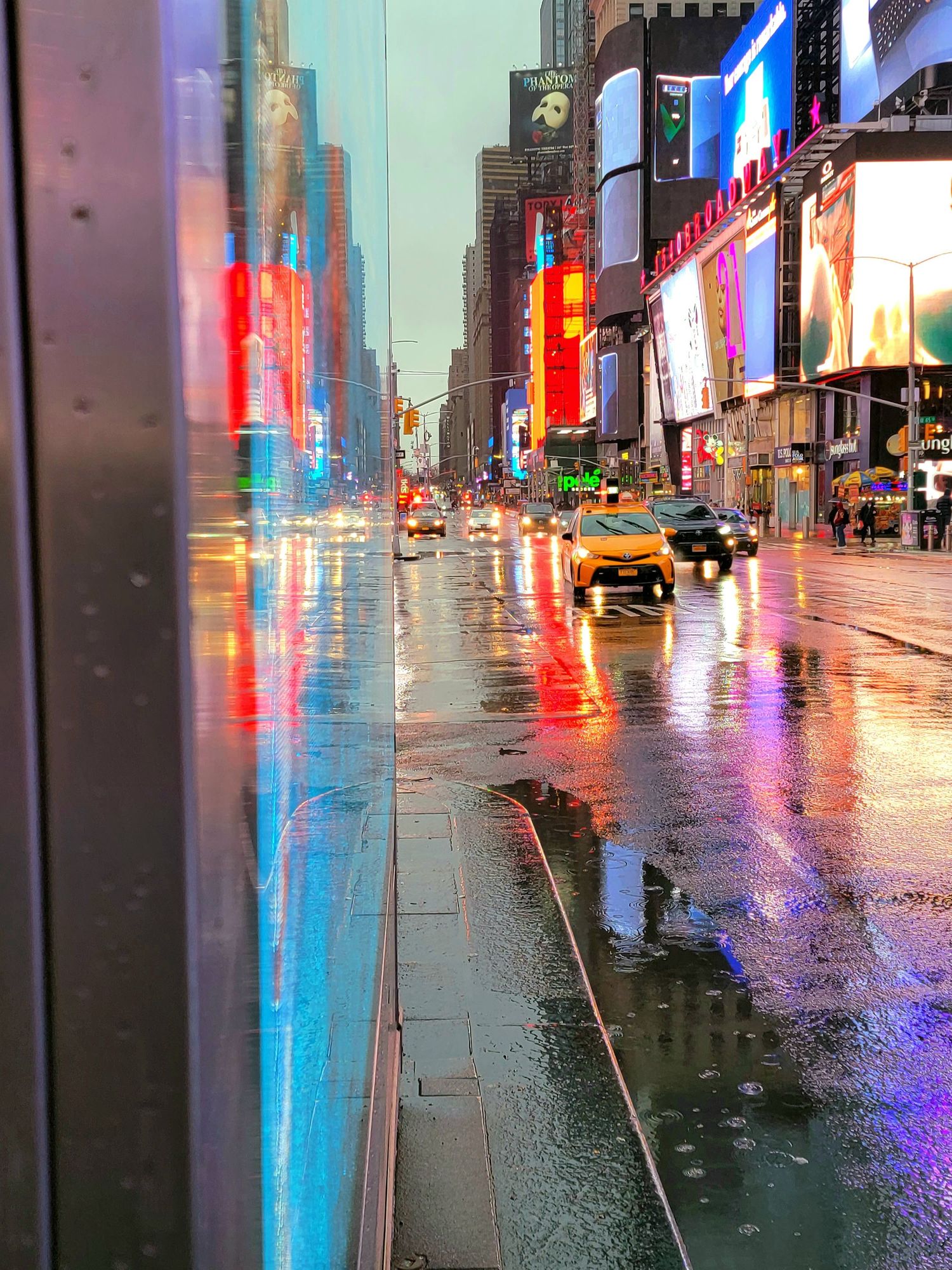 Wet city street reflecting colorful neon lights from surrounding buildings and advertisements.