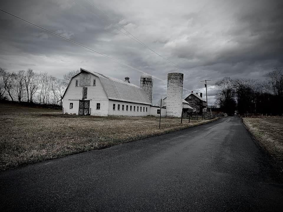 A stark black and white panorama of rural buildings along an empty road under overcast skies.