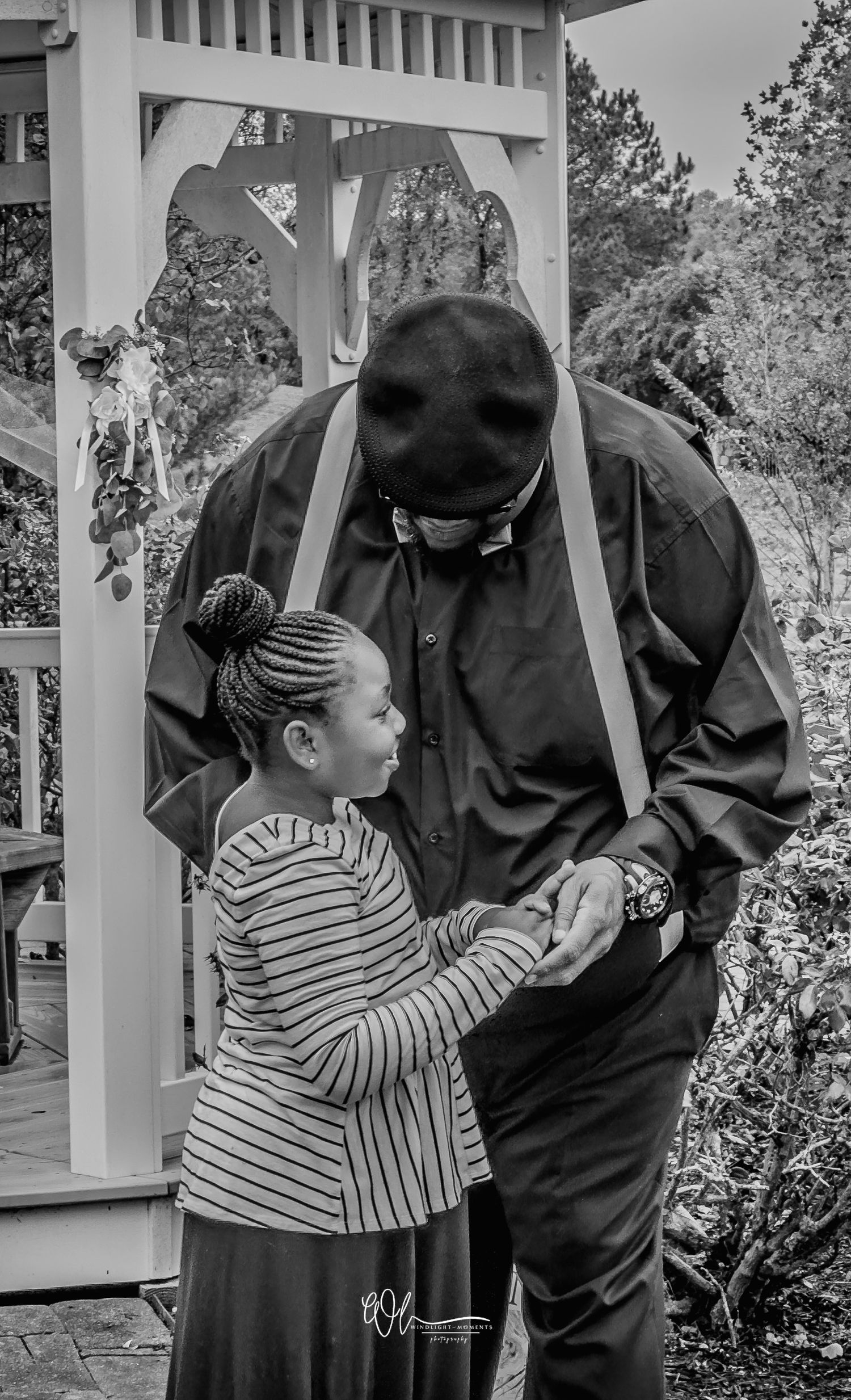 A child in a striped shirt interacts with someone wearing black clothing in a garden setting.