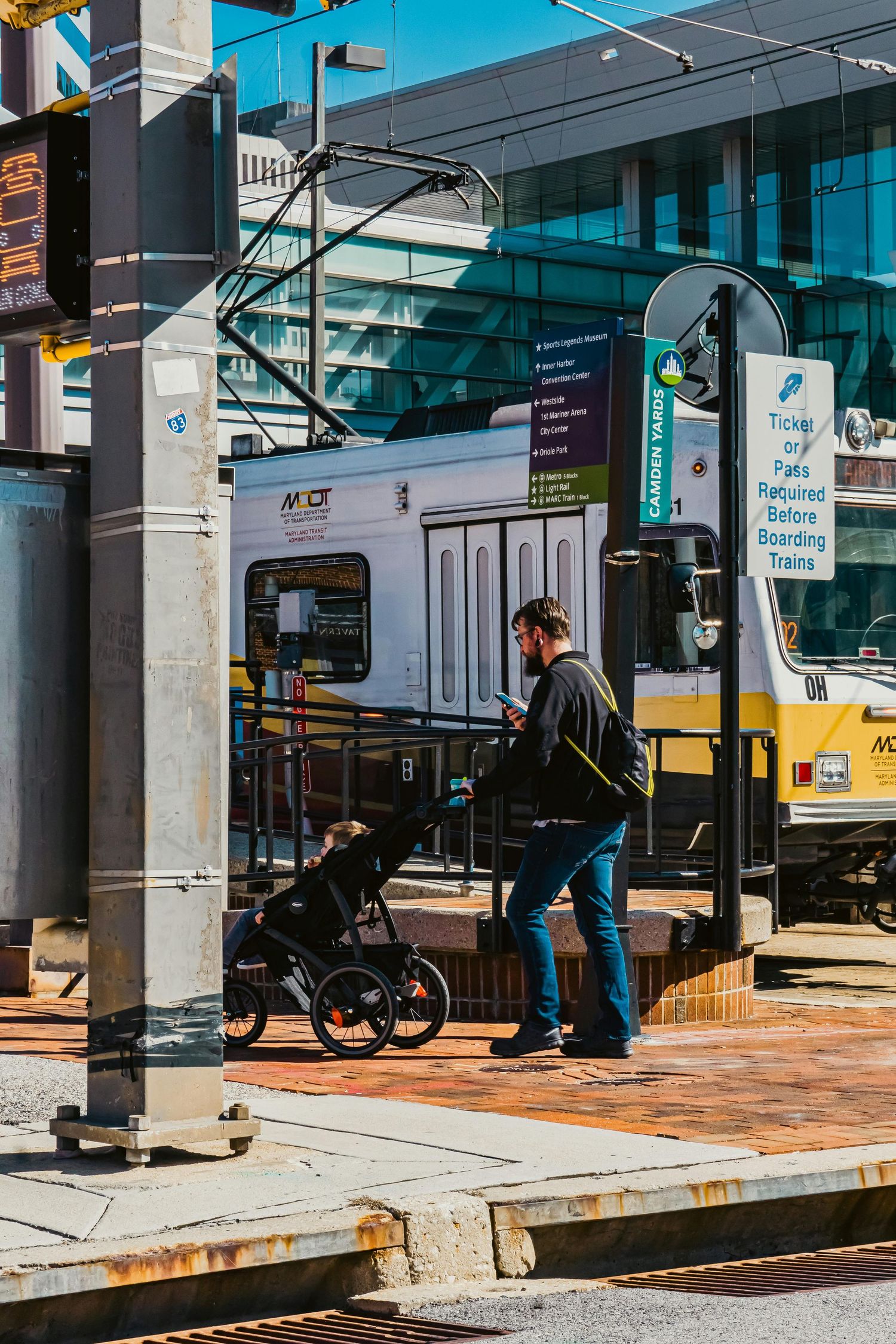 Person with stroller waiting at urban transit stop on sunny day.