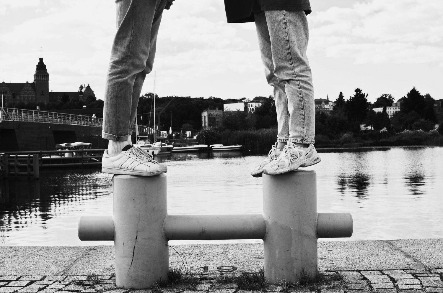 Legs in sneakers standing on a concrete pipe near water.