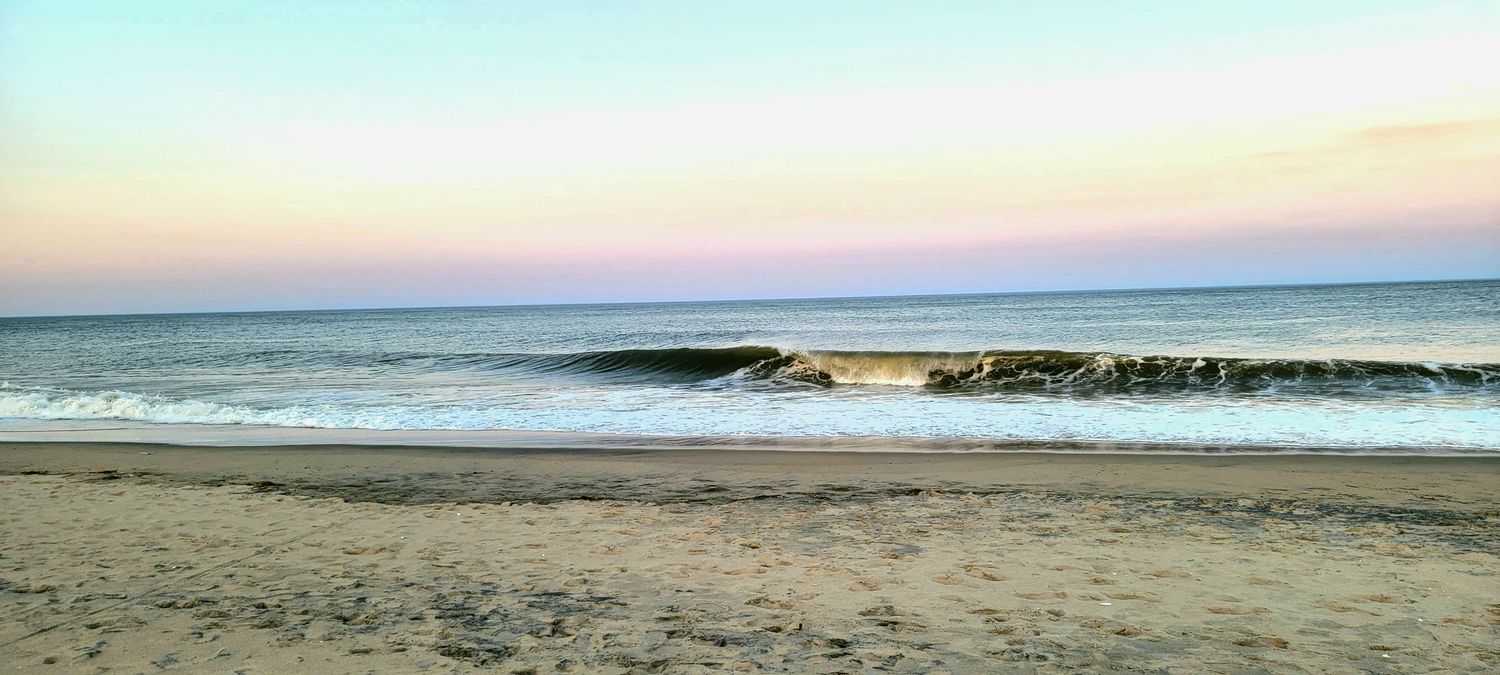 A serene panoramic view of an ocean beach at sunset with gentle waves rolling in.