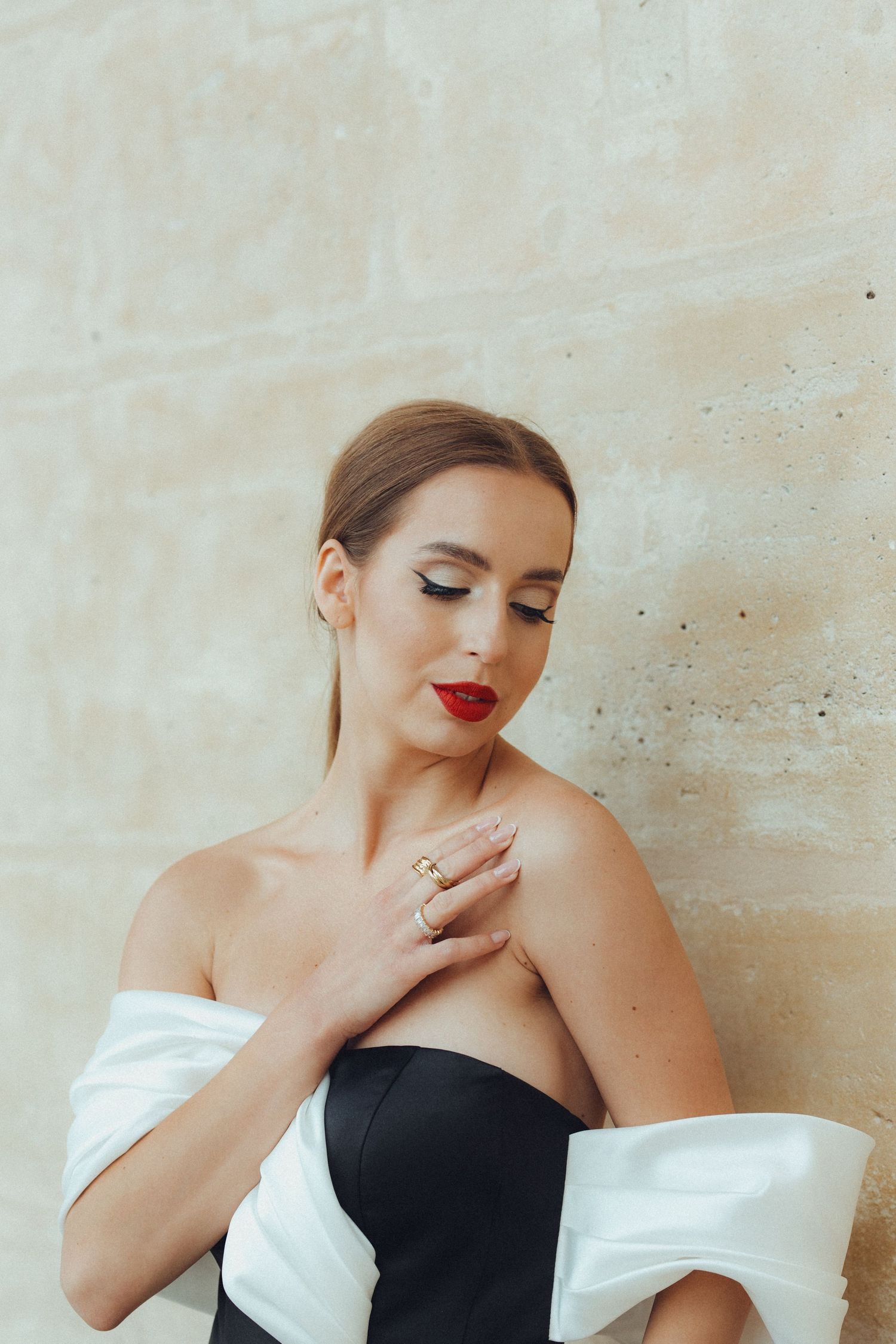 Elegant portrait of woman in black and white dress with bold red lipstick against light wall.