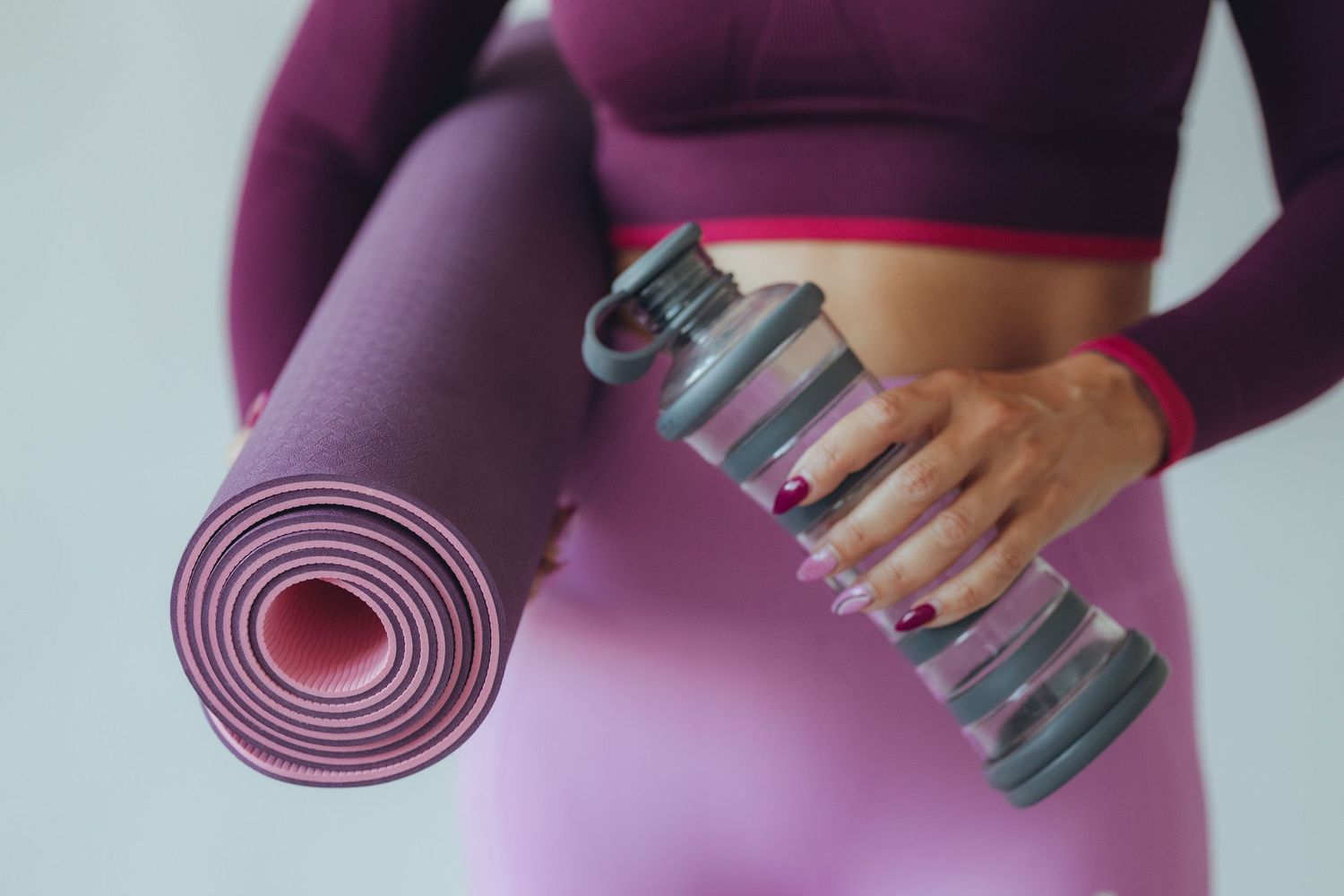 Person holding purple yoga mat and water bottle in workout attire.