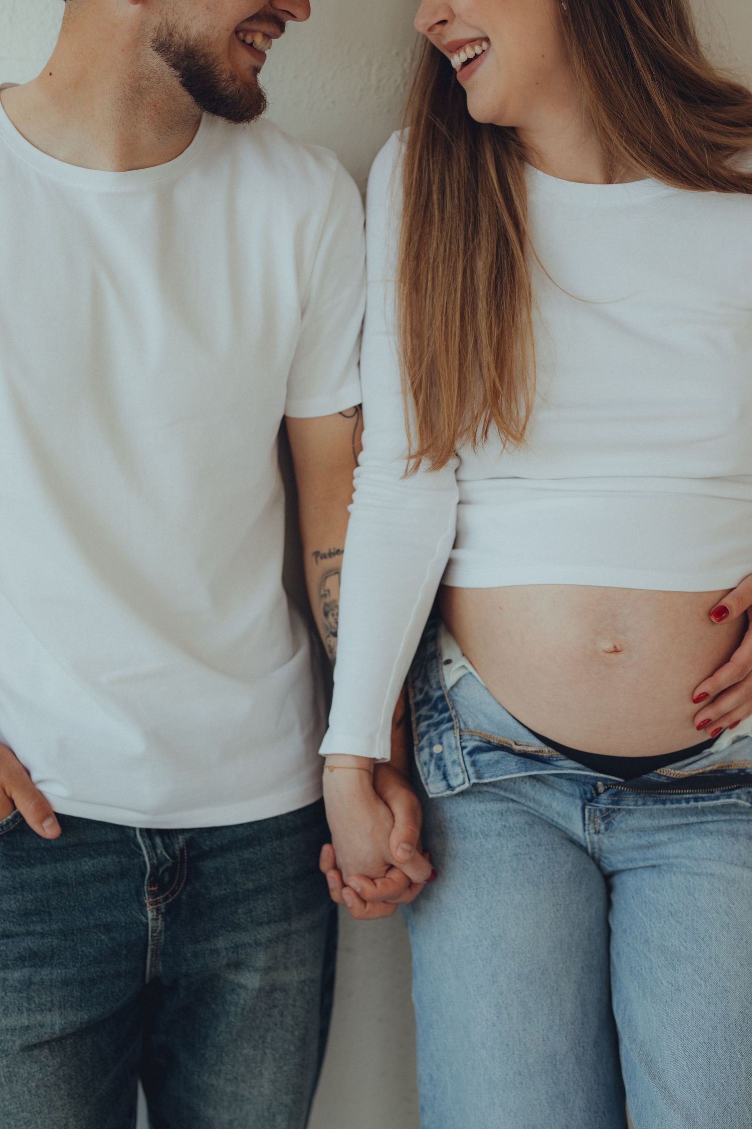 A couple in jeans and white tops holding hands and laughing together in a casual intimate photoshoot.