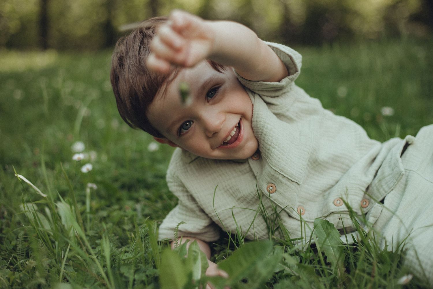 A playful child lying in spring grass with blooming flowers.