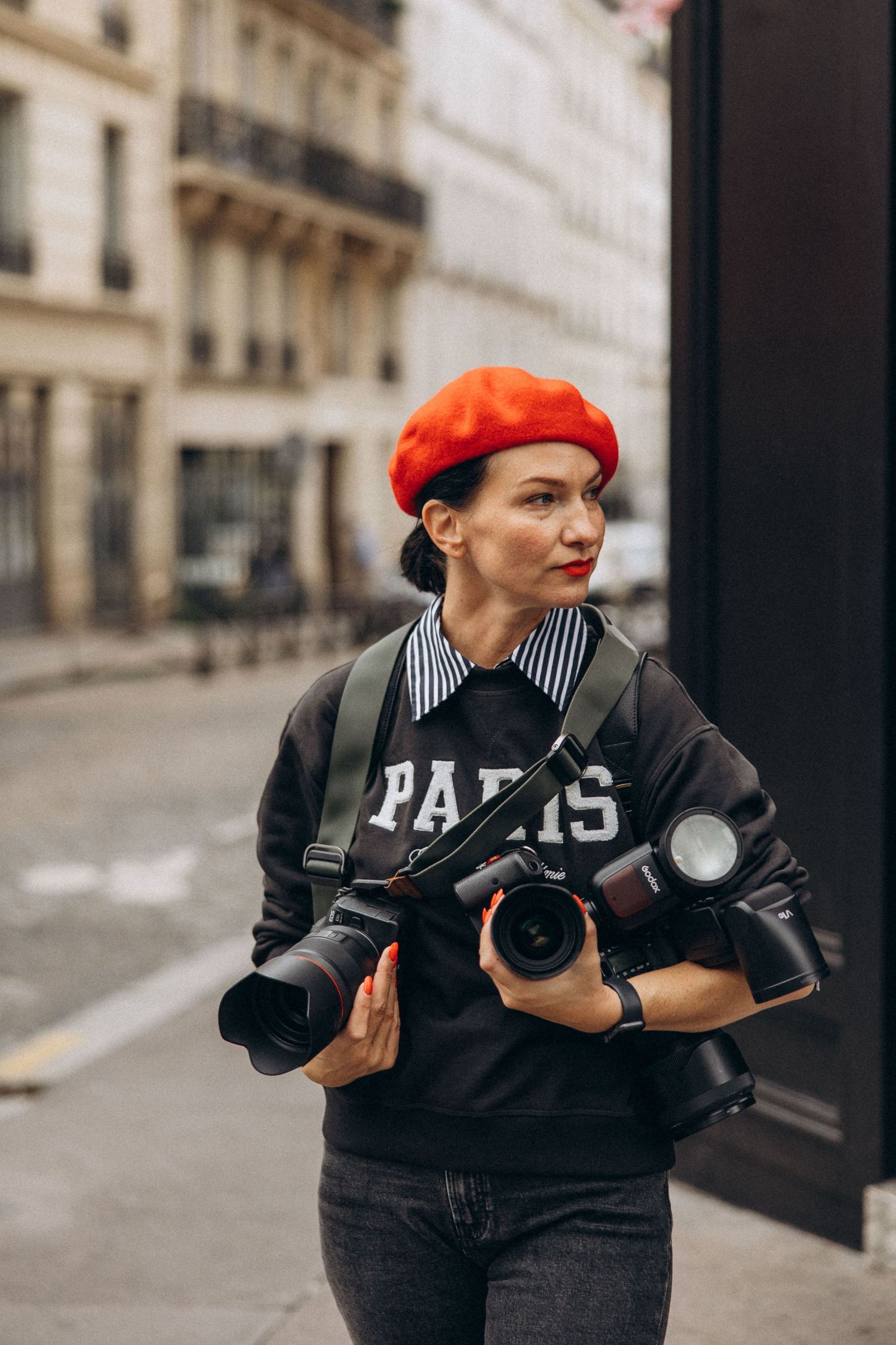 A photographer in black attire and red beret captures images on a Parisian street.
