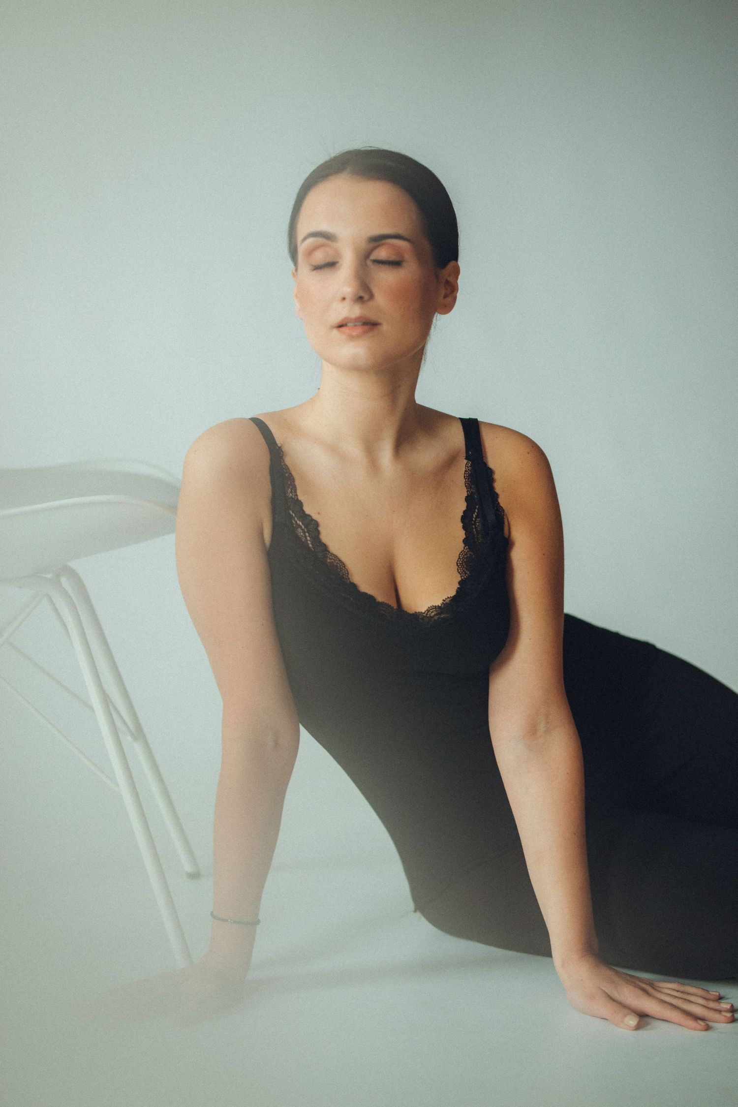 Elegant boudoir portrait in black bodysuit against white background.
