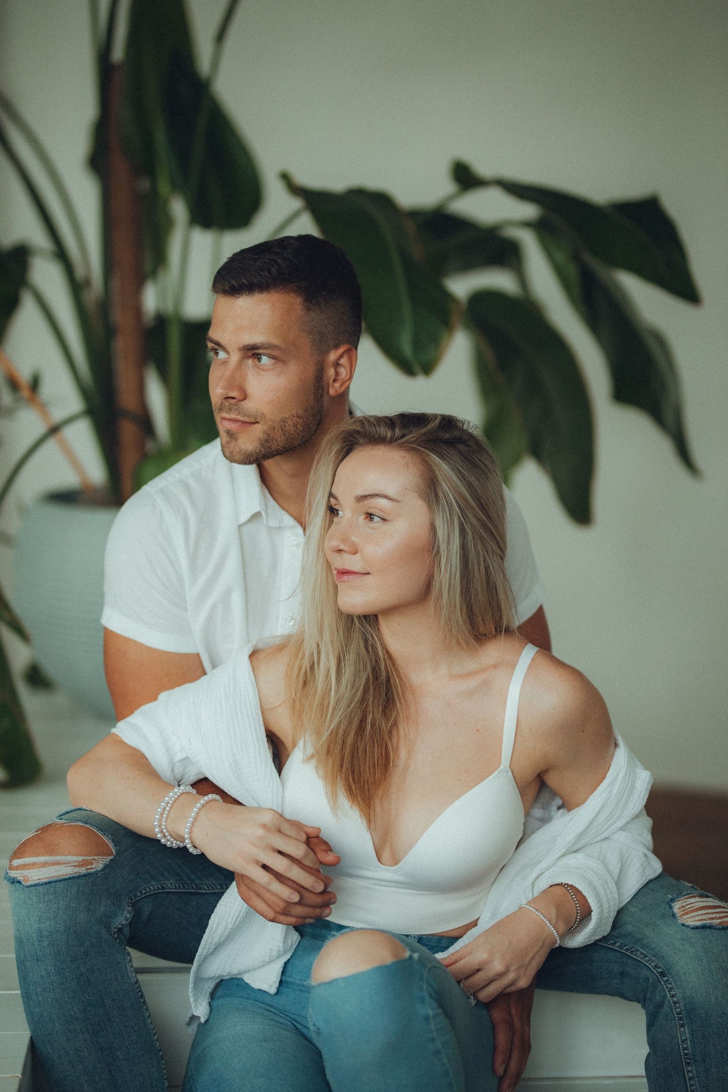 A couple relaxes on a white couch with tropical plants in the background.