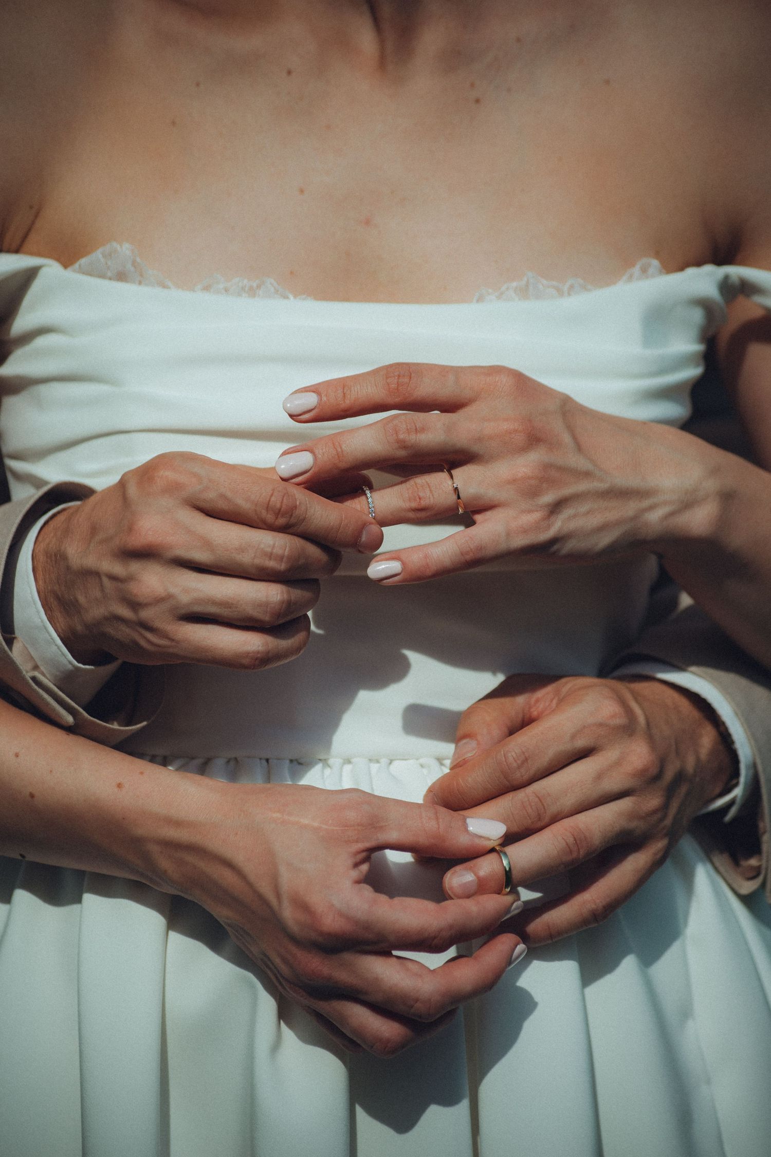 Close-up of hands embracing around a white dress, showing delicate touches and light-colored nail polish.