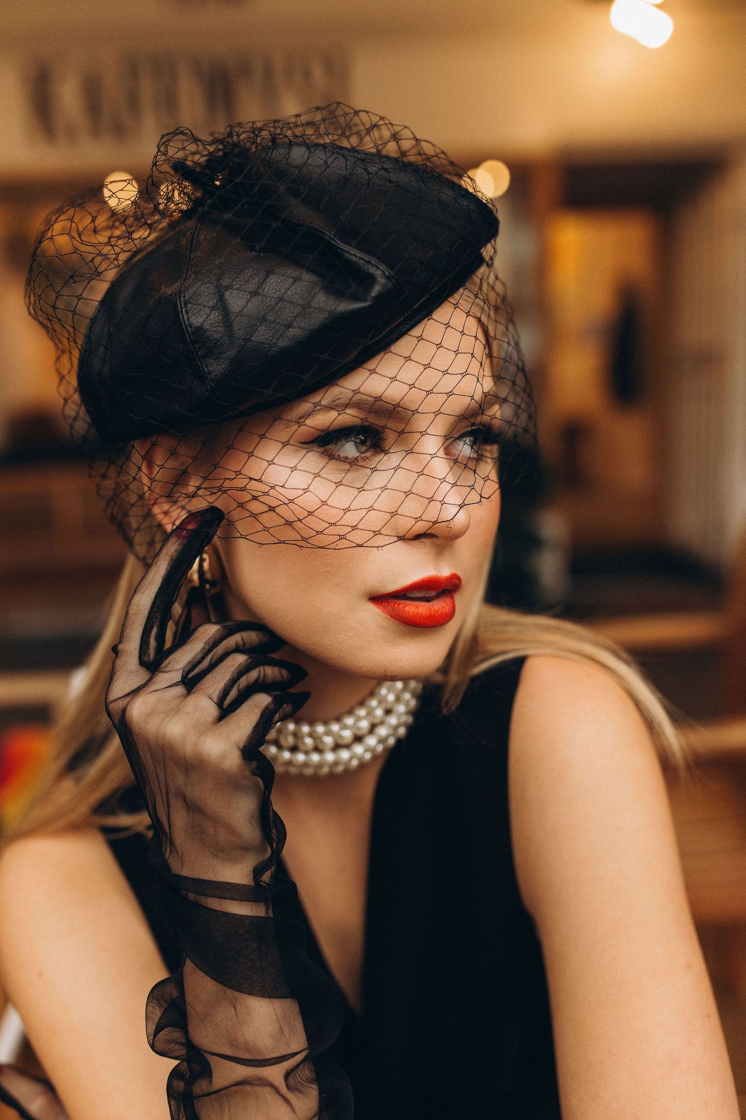 Vintage-inspired portrait with black veil hat, pearls and dramatic red lipstick in warm lighting.