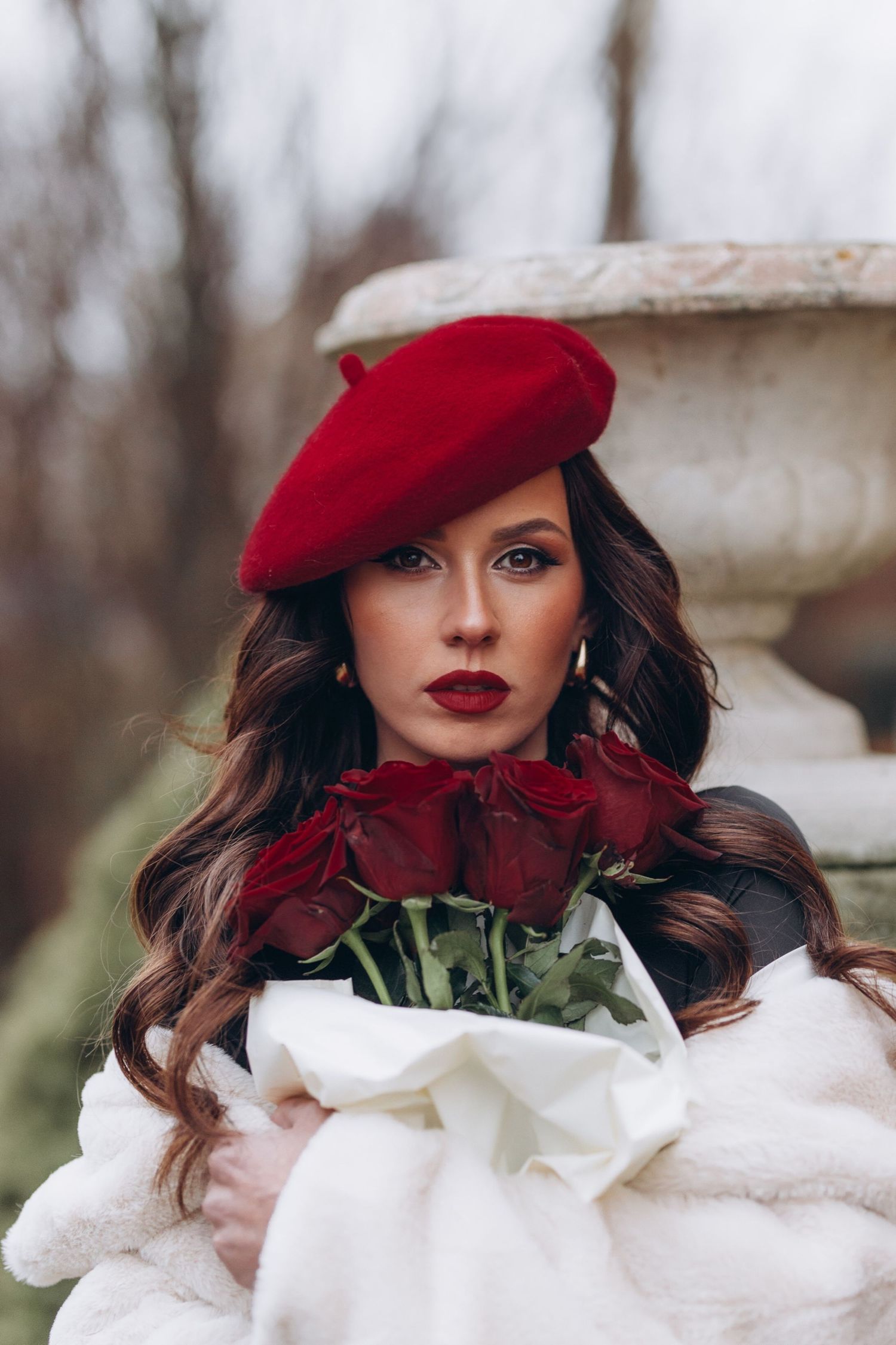 A glamorous winter portrait featuring red roses and white fur with a red beret against a snowy background.