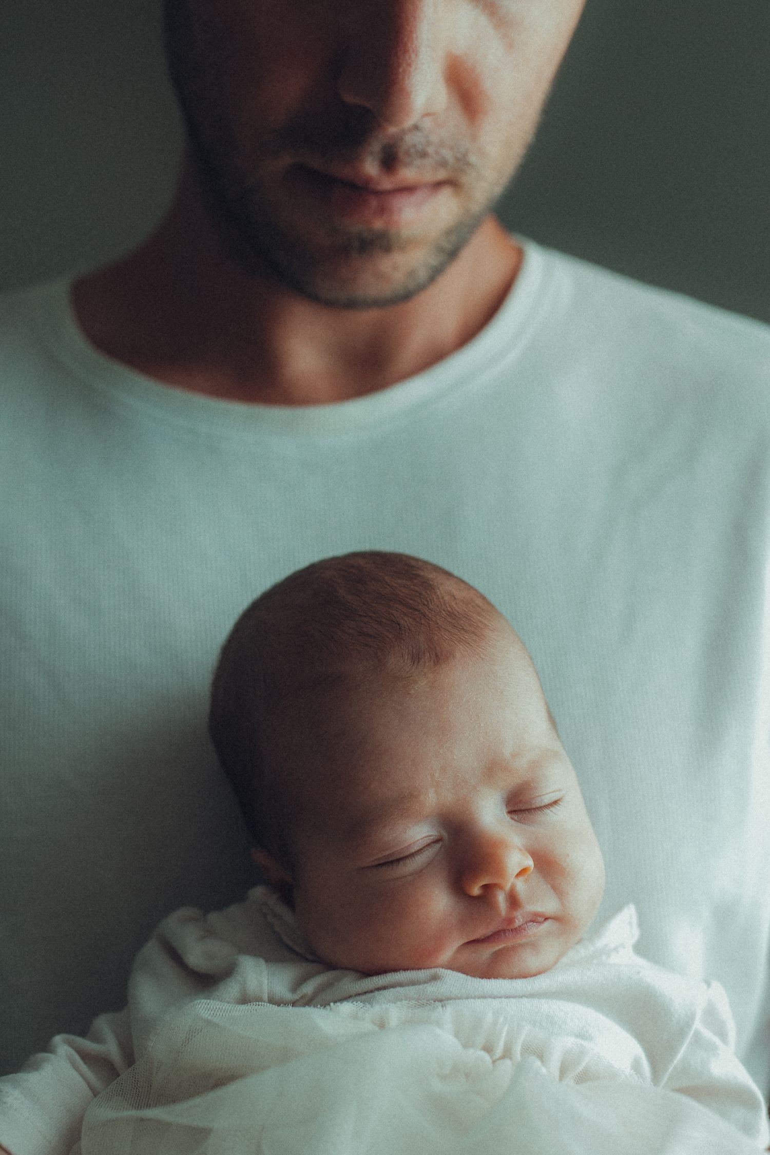 Peaceful sleeping newborn baby resting on person wearing white shirt.