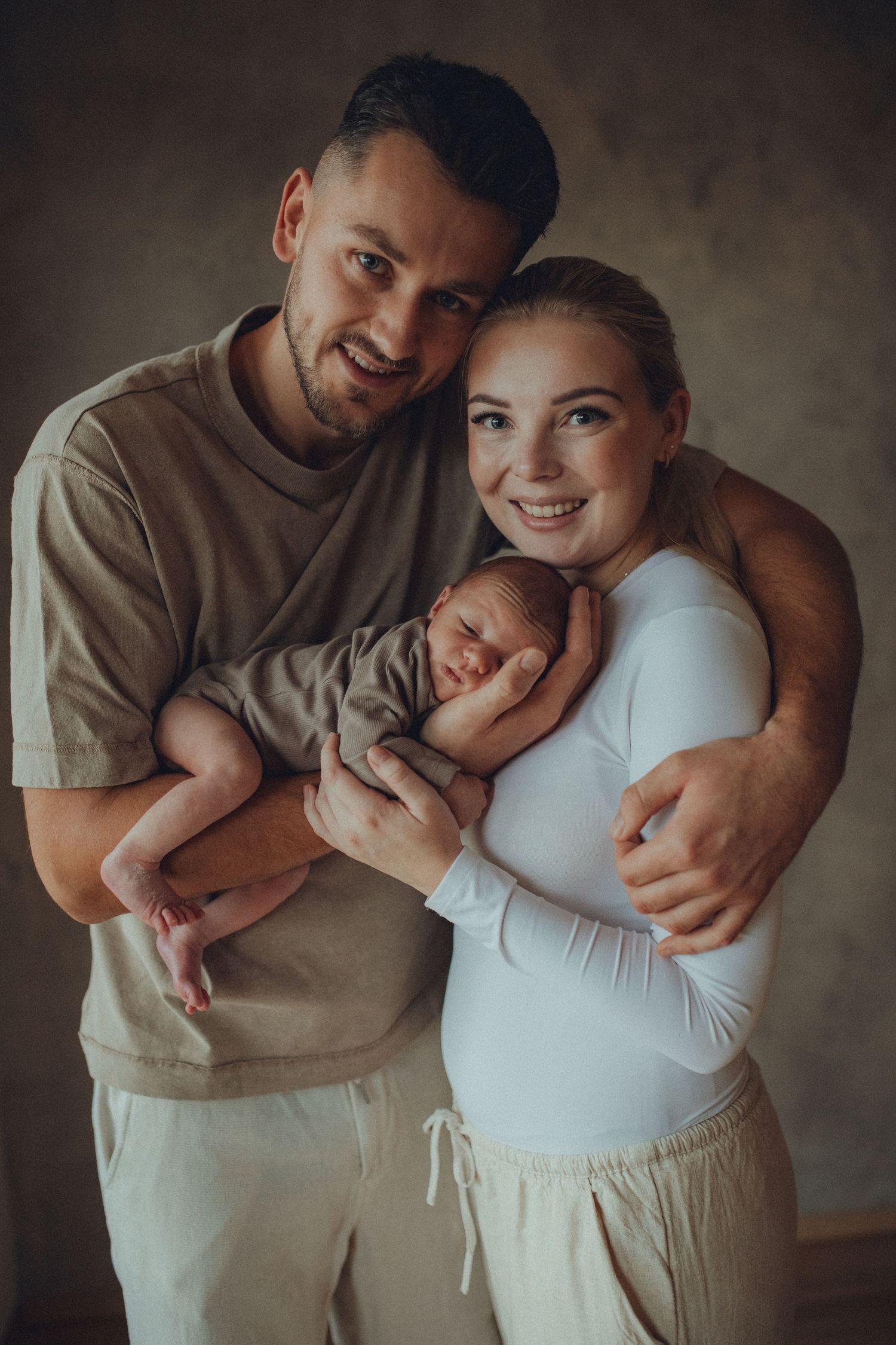 A loving couple embraces in a series of intimate maternity photos wearing neutral beige and white clothing.